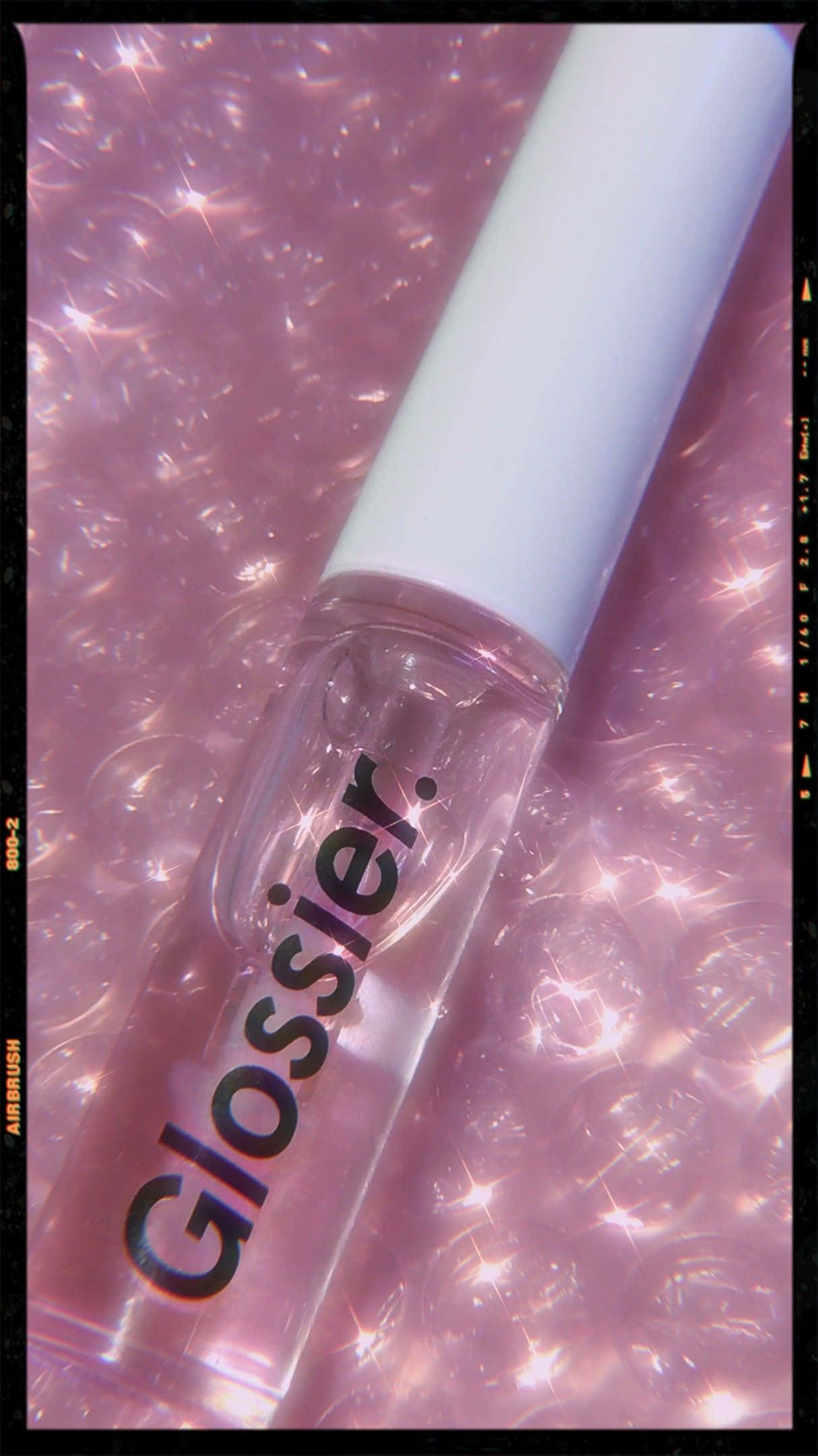 Cosmetic 桌布 壁紙 — 一個帶白色蓋的透明 Glossier 唇彩瓶放在閃爍的粉紅色泡泡背景上，帶有菲林顆粒感。