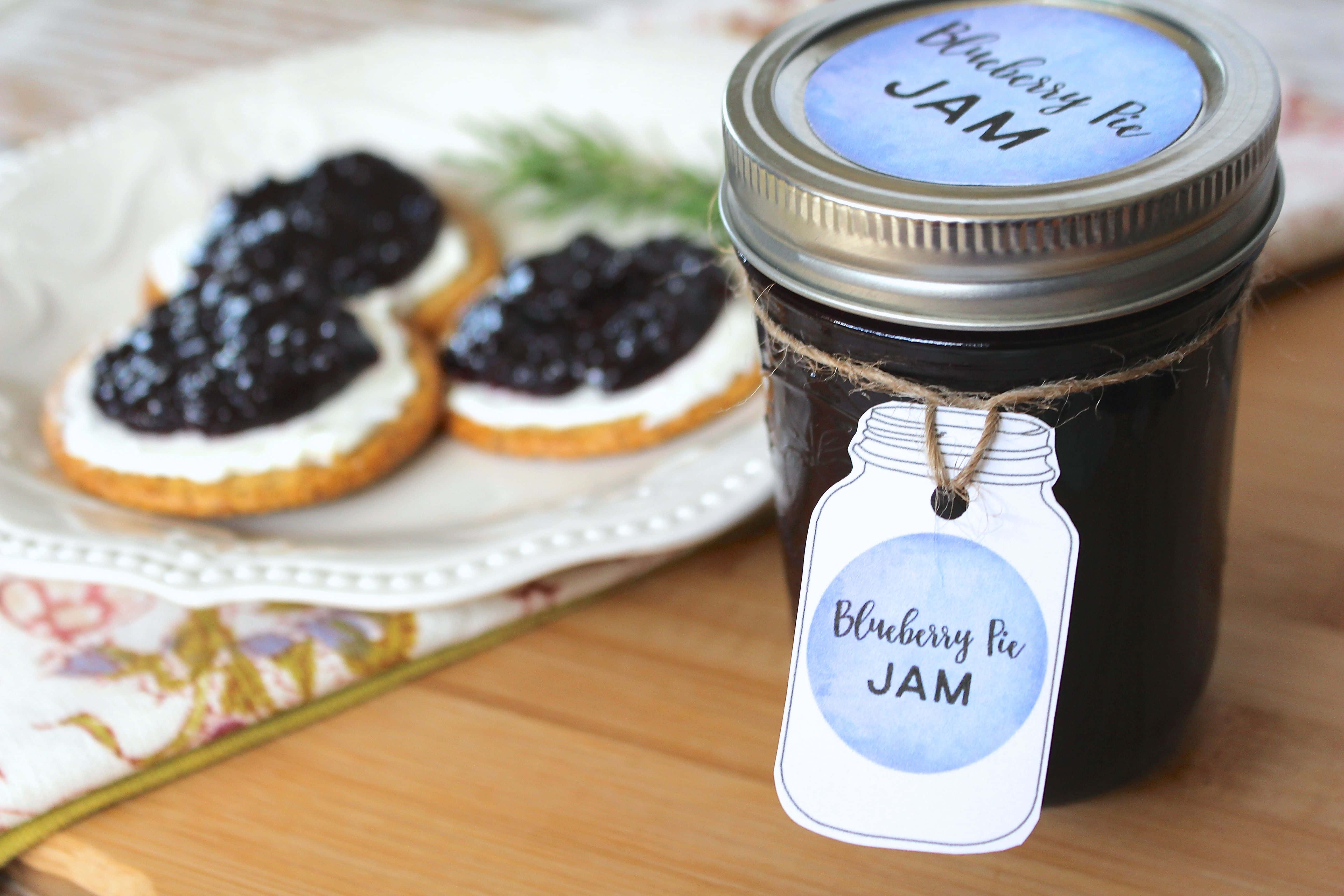 Blueberry Jam 桌布 壁紙 — 一個帶麻繩標籤的藍莓批果醬罐，旁邊放著塗上果醬的餅乾，在木桌上。