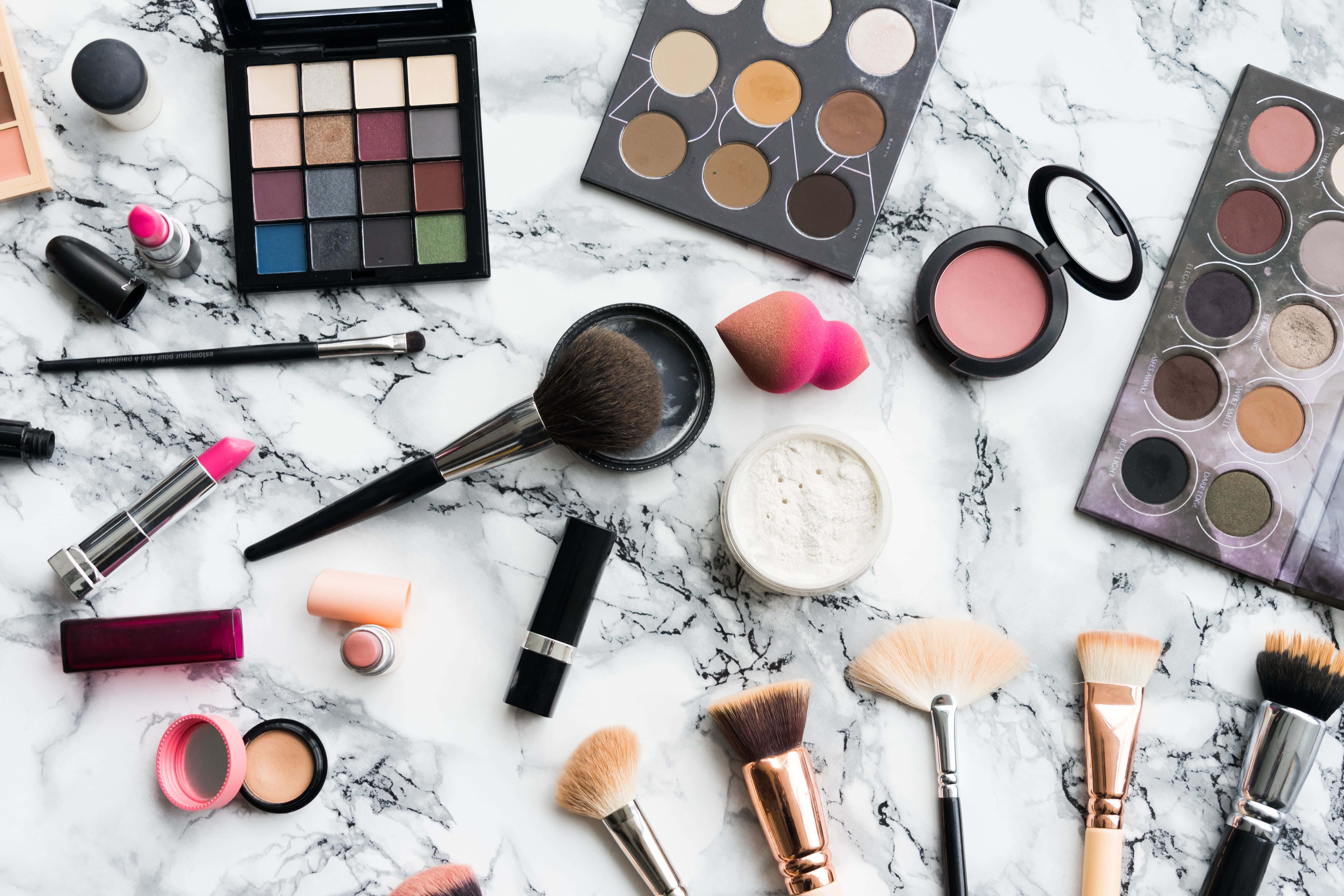 Cosmetic 桌布 壁紙 — 一個平鋪佈局，各種化妝品如眼影盤、刷子和唇膏散落在白色大理石表面上。