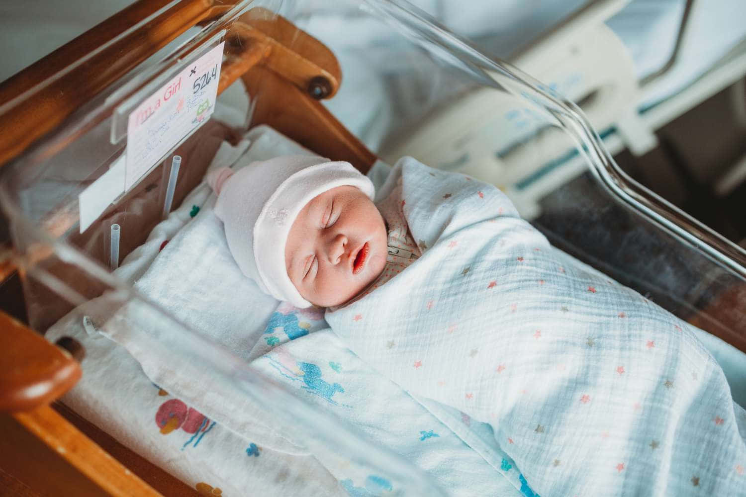 Newborn Baby 桌布 壁紙 — 一個平靜的新生女嬰在醫院的嬰兒床裡，被柔軟的圖案毛毯包裹著，睡得香甜。
