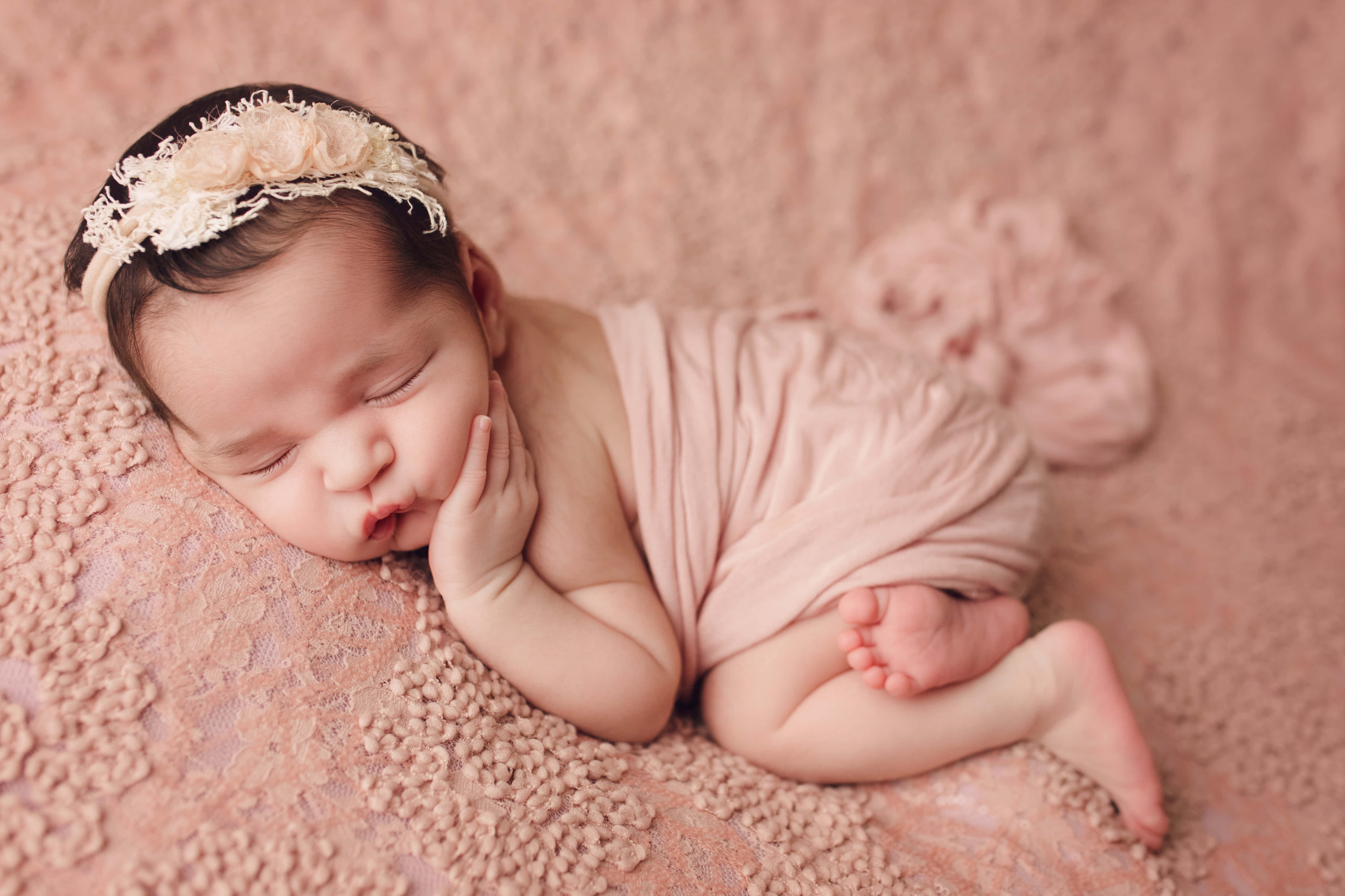 Newborn Baby 桌布 壁紙 — 一個平靜的新生嬰兒在柔軟的粉紅色紋理毛毯上安詳地睡覺，戴著精緻的蕾絲頭帶。