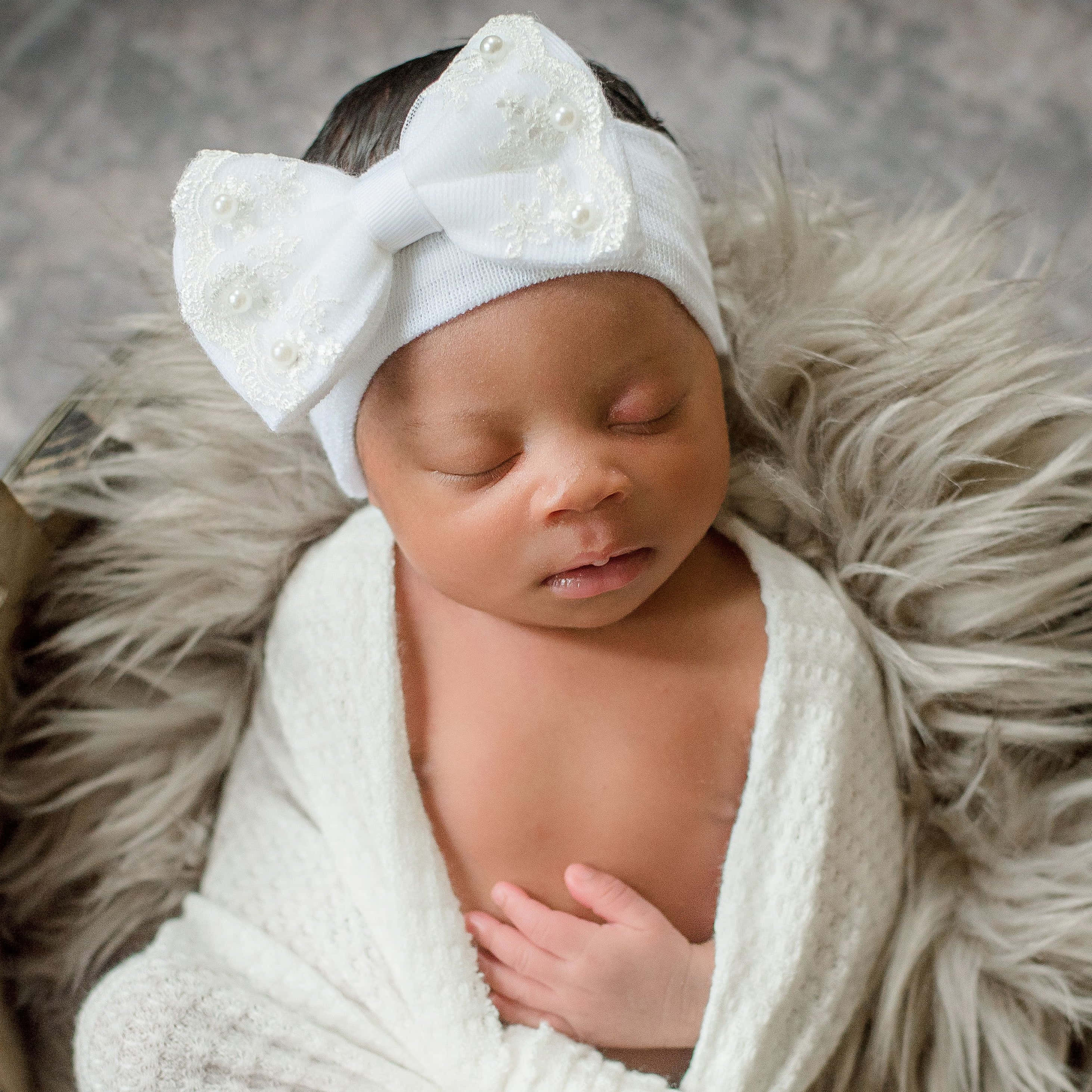 Newborn Baby 桌布 壁紙 — 一個平靜的新生嬰兒被柔軟的白色針織布包裹著，戴著精緻的白色蝴蝶結頭帶，安然入睡。