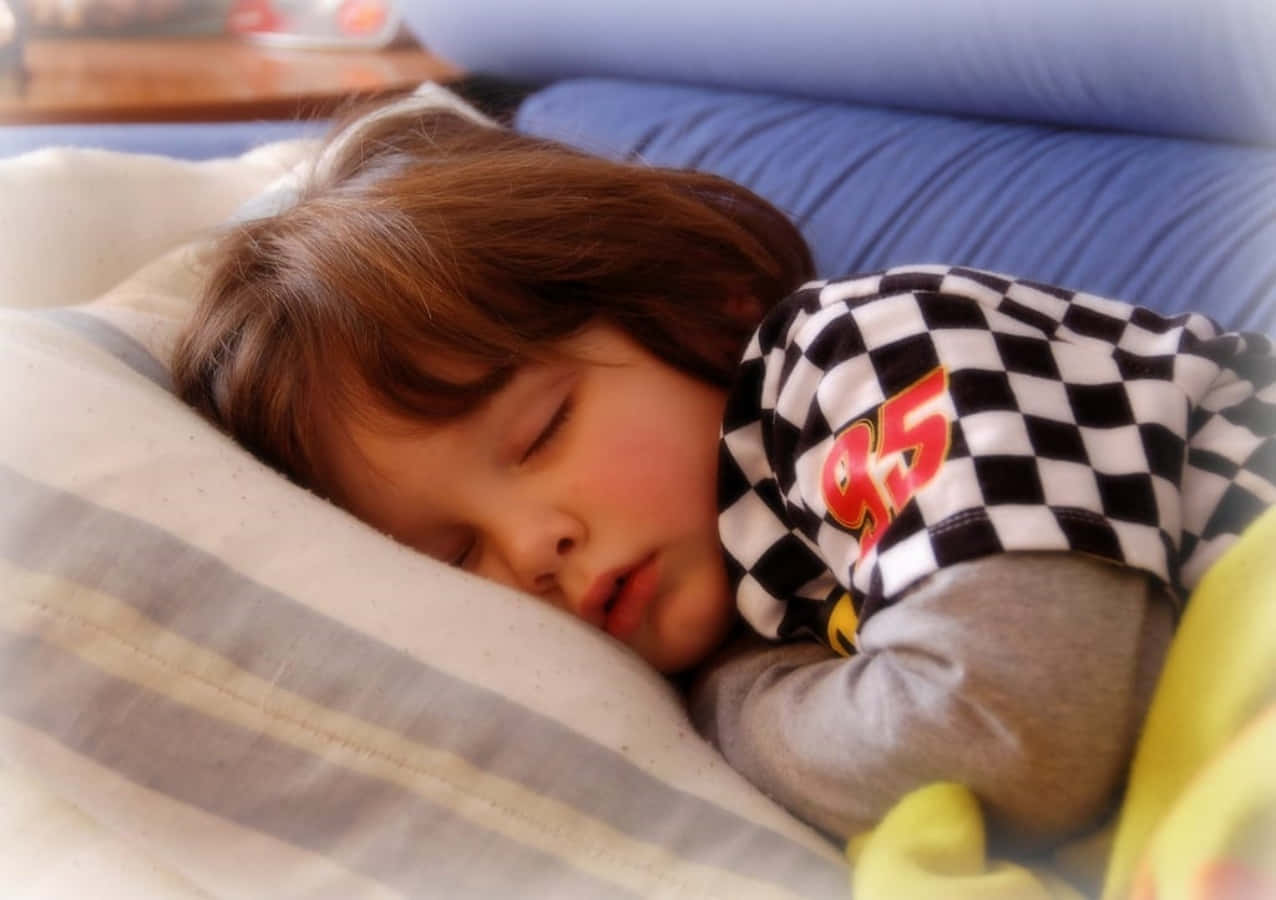 Sleep 桌布 壁紙 — 一個年幼的孩子在條紋枕頭上安詳地睡著，穿著格仔賽車睡衣上衣。