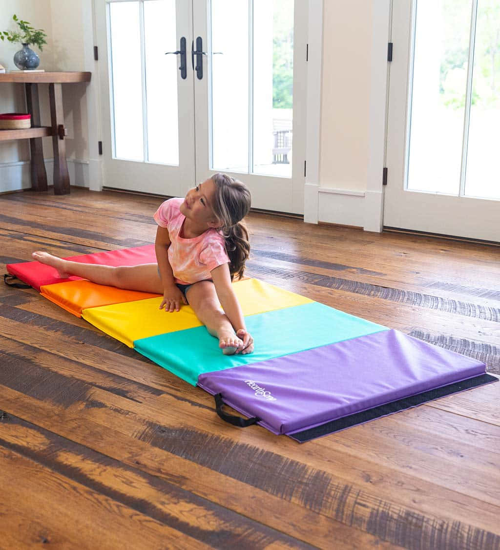 Gymnastics Mat 桌布 壁紙 — 一個年輕女孩在明亮的陽光房間裏，在鋪在硬木地板上的彩虹色體操墊上伸展身體。