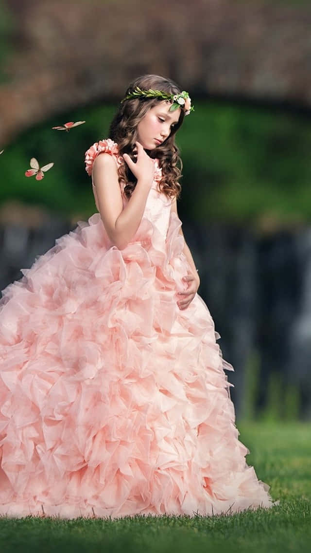 Butterfly Dress 桌布 壁紙 — 一個年輕女孩穿著寬鬆的桃色荷葉邊連衣裙，站在草地上，戴著花冠，蝴蝶在附近飛舞。