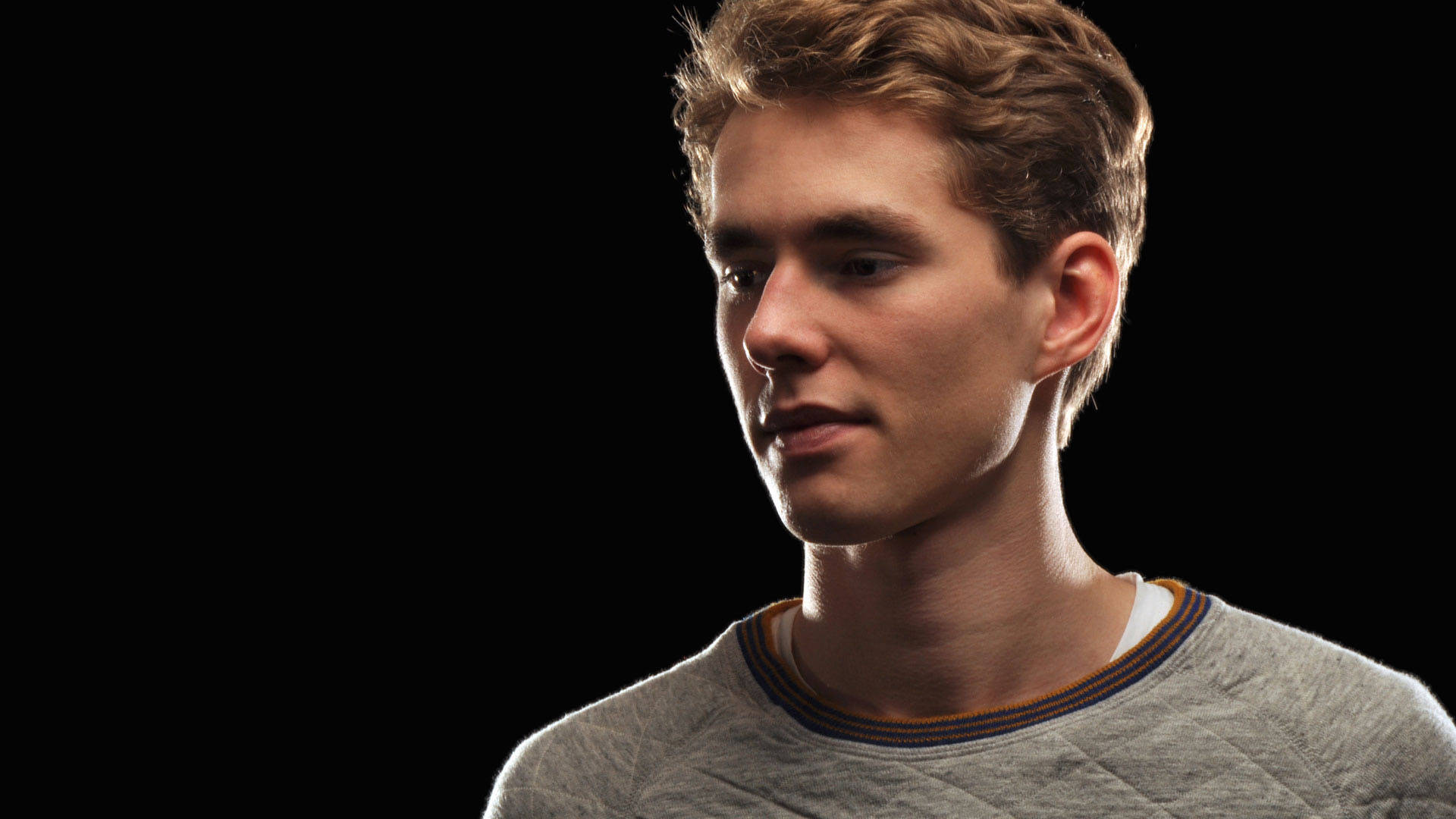 Lost Frequencies DJ 壁紙 — 一個年輕男子，一頭凌亂的棕色頭髮，在純黑背景下若有所思地凝視著。