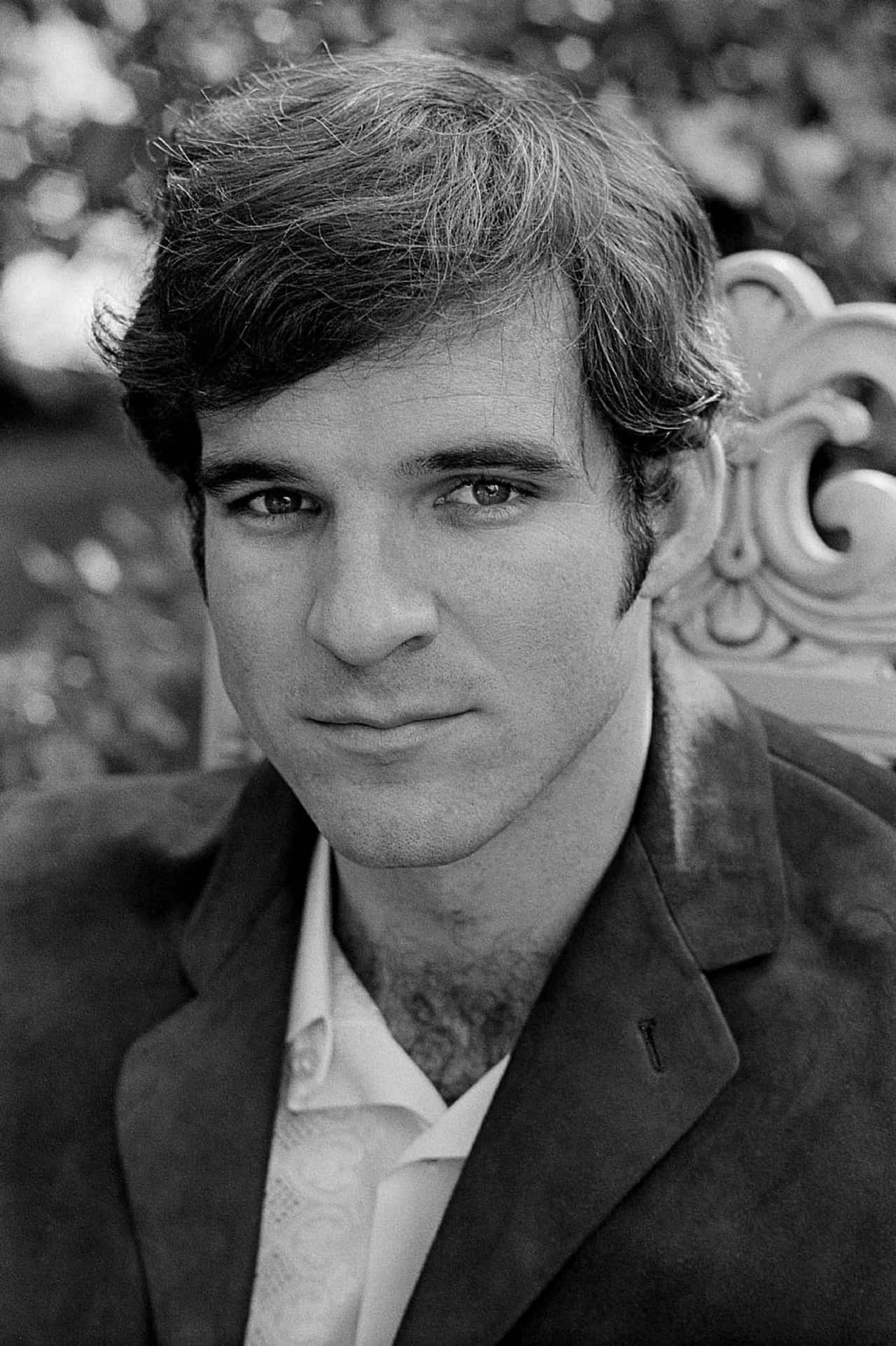 steve martin 桌布 壁紙 — 一個年輕黑髮男子坐在華麗椅子上，眼神銳利直視鏡頭的黑白肖像。