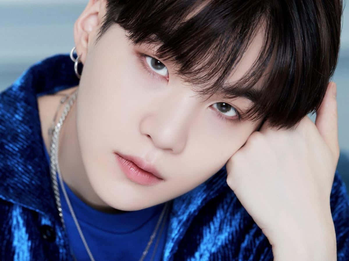 Suga 桌布 壁紙 — 一個年輕黑髮男子的特寫肖像，他眼神銳利，穿著質感藍色外套，手托著頭。