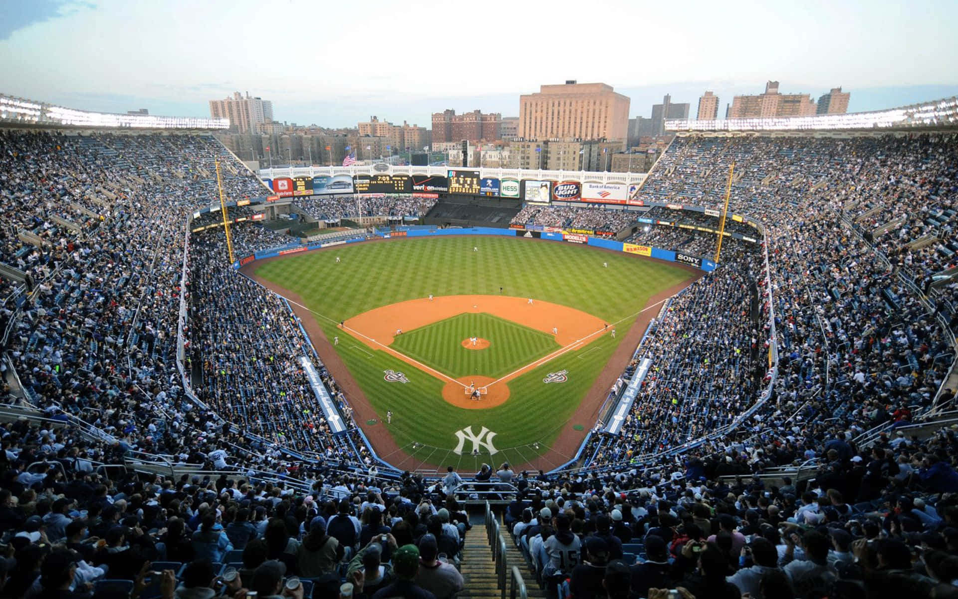 Baseball Stadium 桌布 壁紙 — 一個座無虛席的棒球場，擁有充滿活力的綠色場地和晴朗天空下熱情歡呼的球迷。
