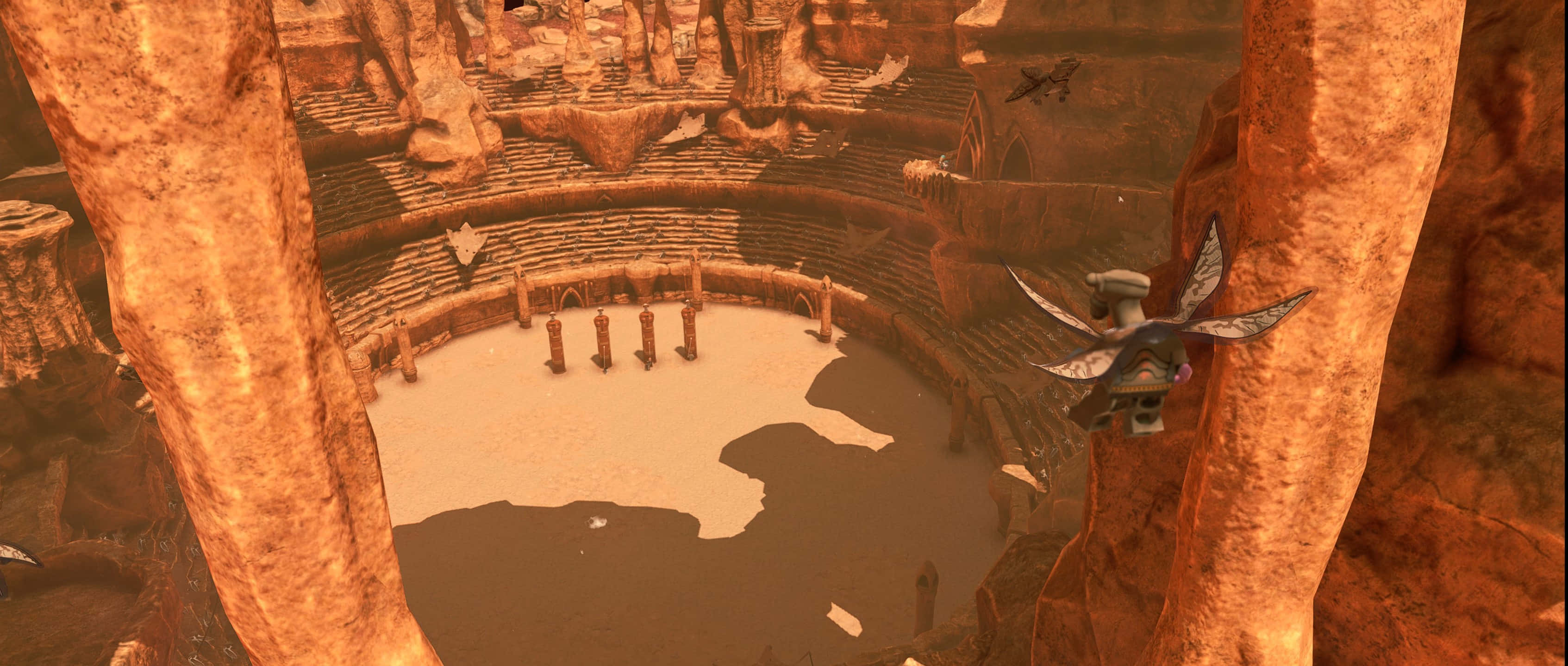 The Geonosian Arena 桌布 壁紙 — 一個廣闊的沙漠圓形劇場，雕刻在橙色岩石中，有一隻類似蜻蜓的生物在柱子附近盤旋。
