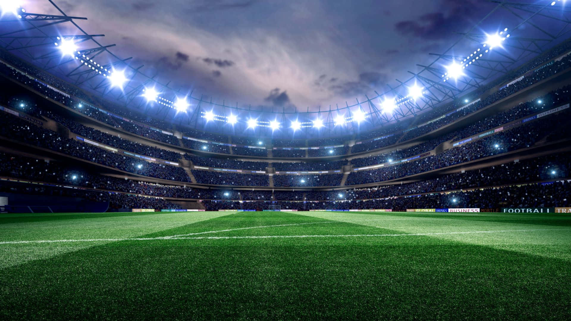 Soccer Stadium 桌布 壁紙 — 一個廣闊的足球場在夜晚被明亮的泛光燈照亮，雲層密佈的天空下座無虛席。