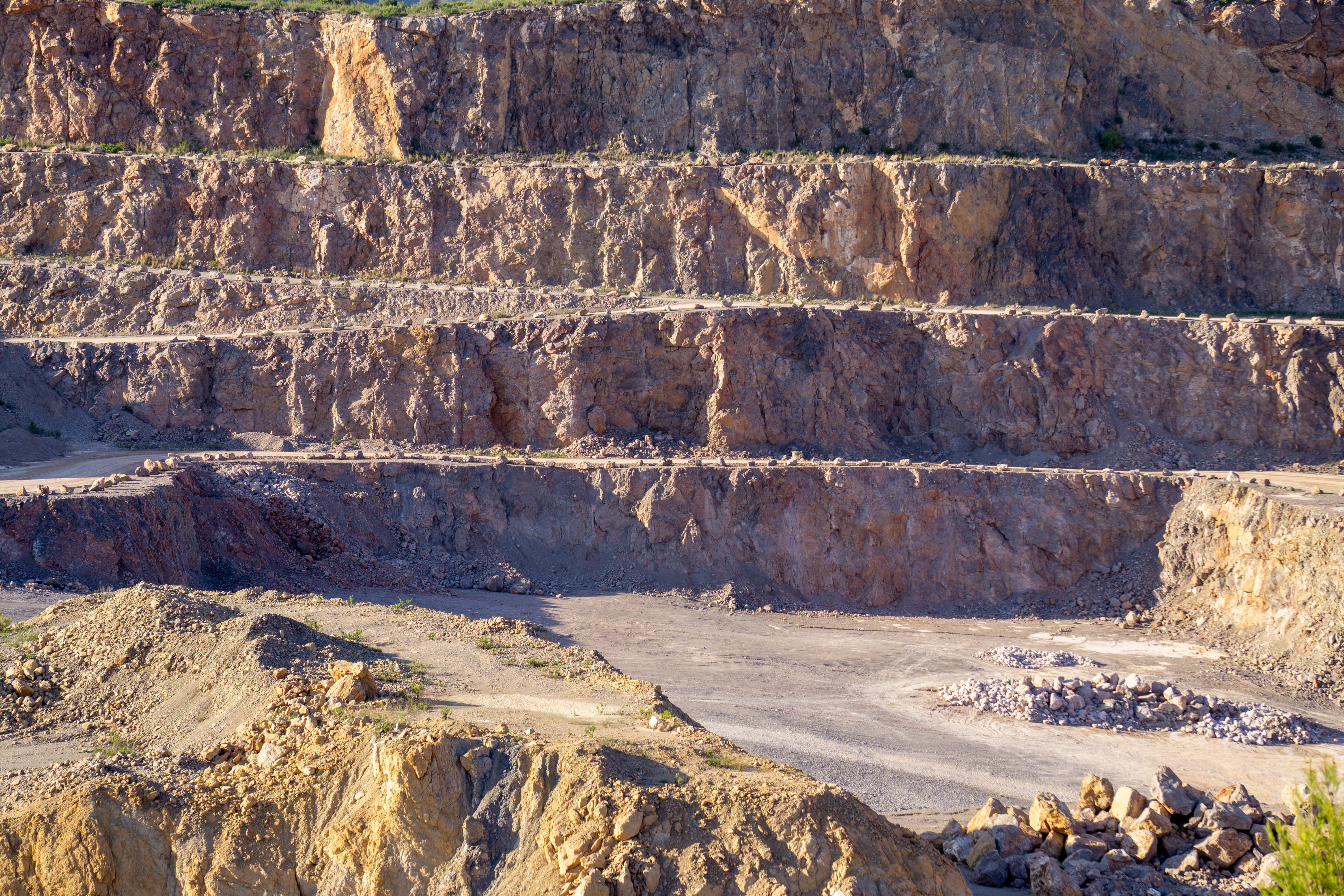 Mining 桌布 壁紙 — 一個廣闊的露天礦場，階梯狀的岩壁在明亮日光下呈現大地色調和粗獷質感。
