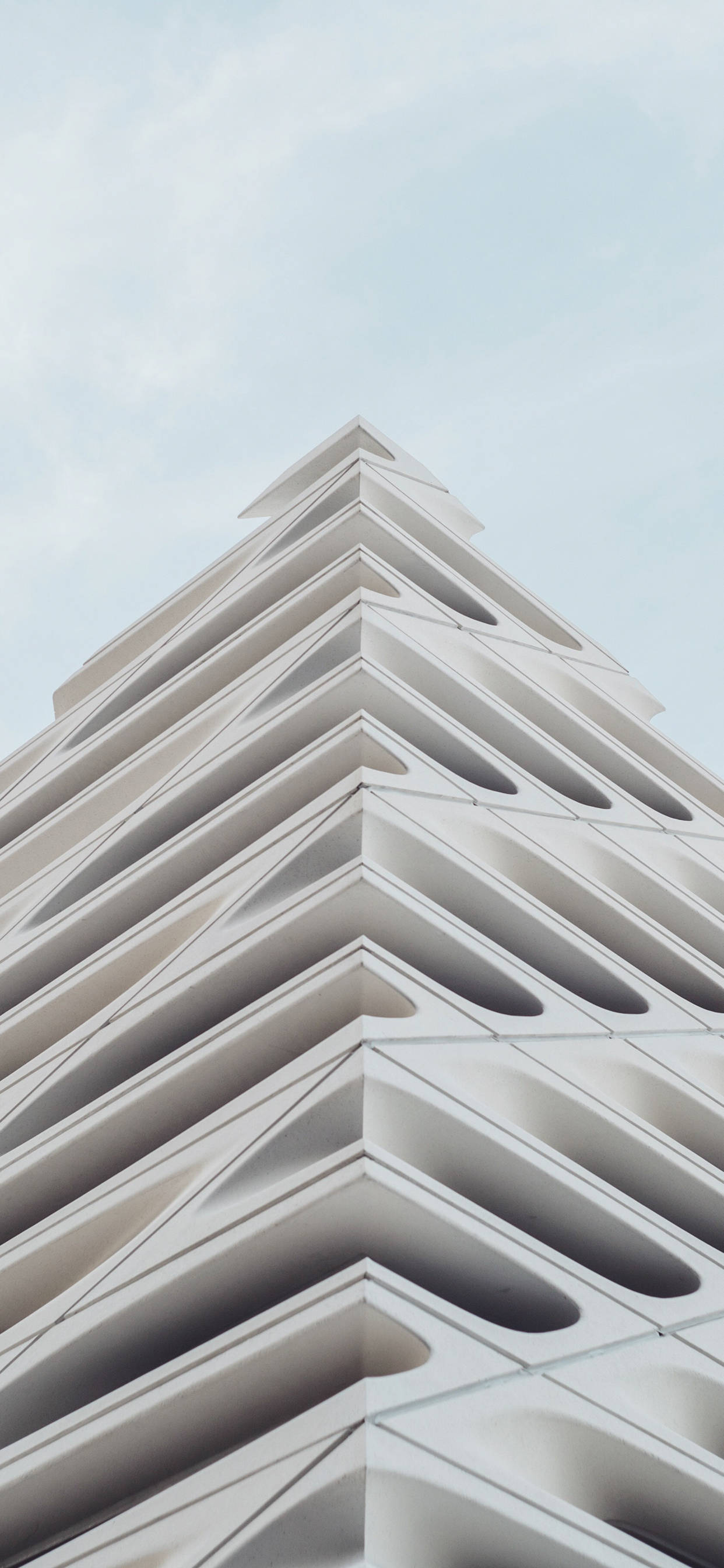 建築 桌布 壁紙 — 一個引人注目的低角度視角，展示現代白色建築結構，帶有重複的幾何人字形圖案，背景是淡色天空。