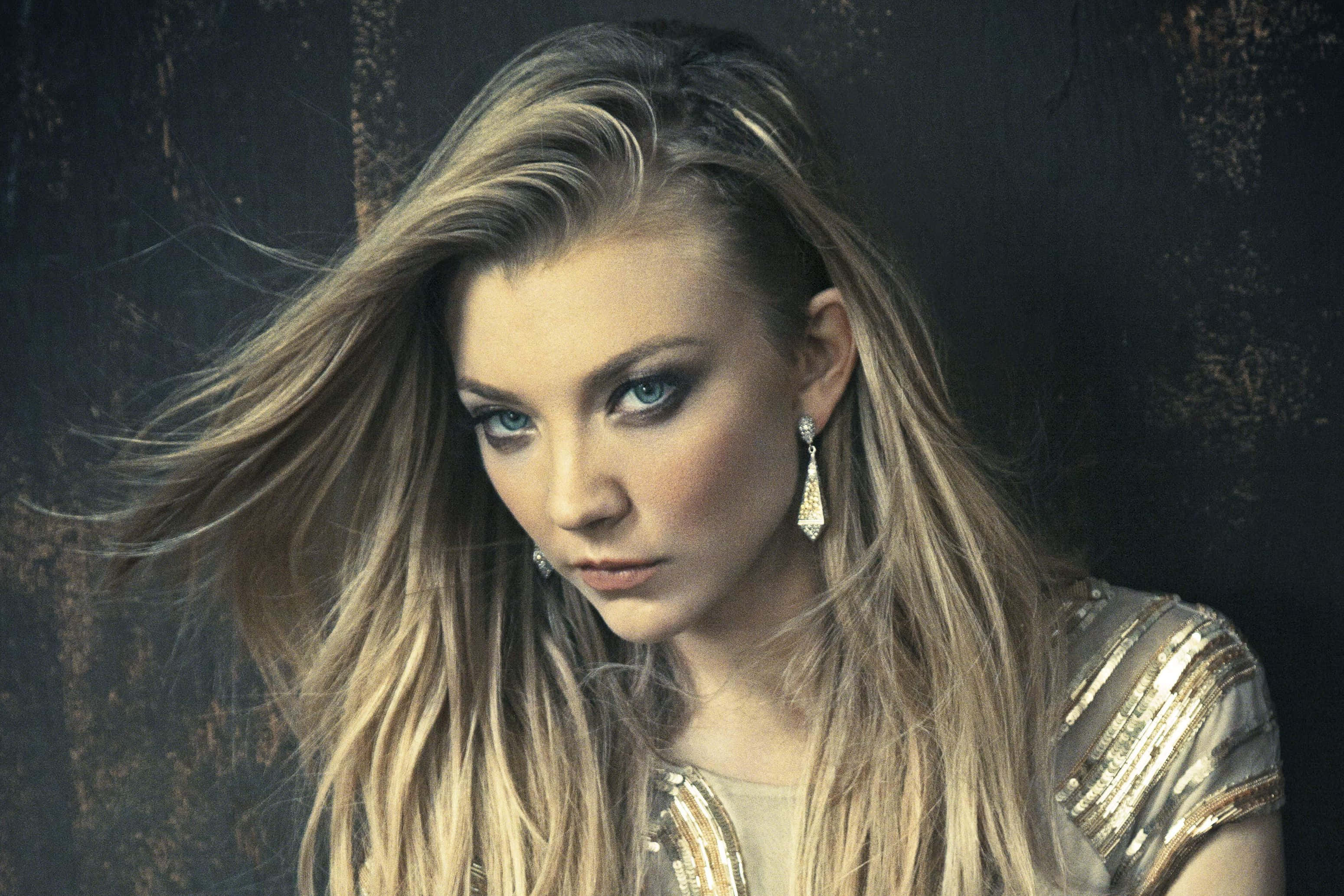 natalie dormer 桌布 壁紙 — 一個引人注目的金髮藍眼女子肖像，頭髮飄逸，背景為深色紋理。