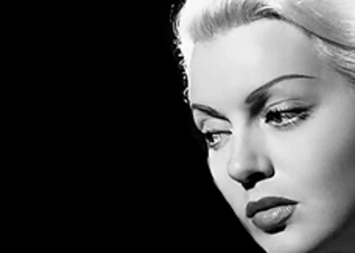 Film Noir 桌布 壁紙 — 一個引人注目的黑白特寫，展現一位迷人女性的臉龐，妝容大膽，光線柔和，背景深色。