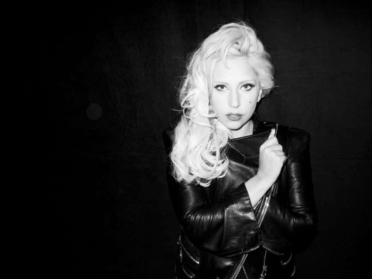 Lady Gaga 桌布 壁紙 — 一個引人注目的黑白肖像，一位擁有豐盈金髮、穿著皮夾克的女性，背景是深色紋理。