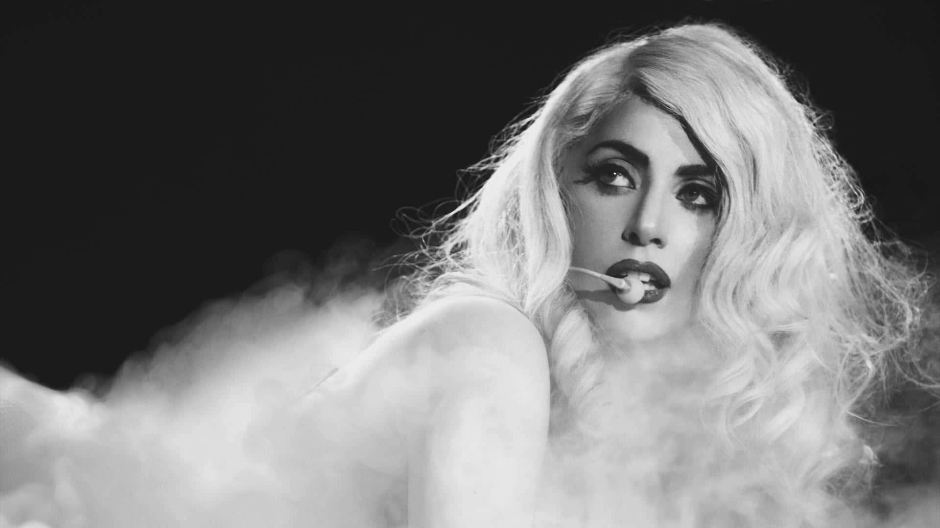Lady Gaga 桌布 壁紙 — 一個引人注目的黑白肖像，一位擁有豐盈金髮的女性從深色背景中旋轉的煙霧中浮現。