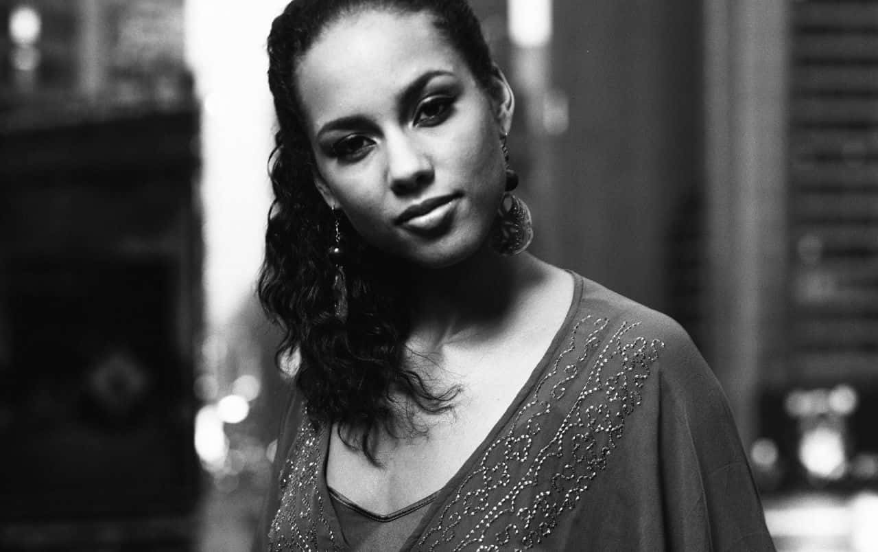 Alicia Keys 桌布 壁紙 — 一個引人注目的黑白肖像，一位擁有捲髮和垂墜耳環的女性在城市環境中直視鏡頭。