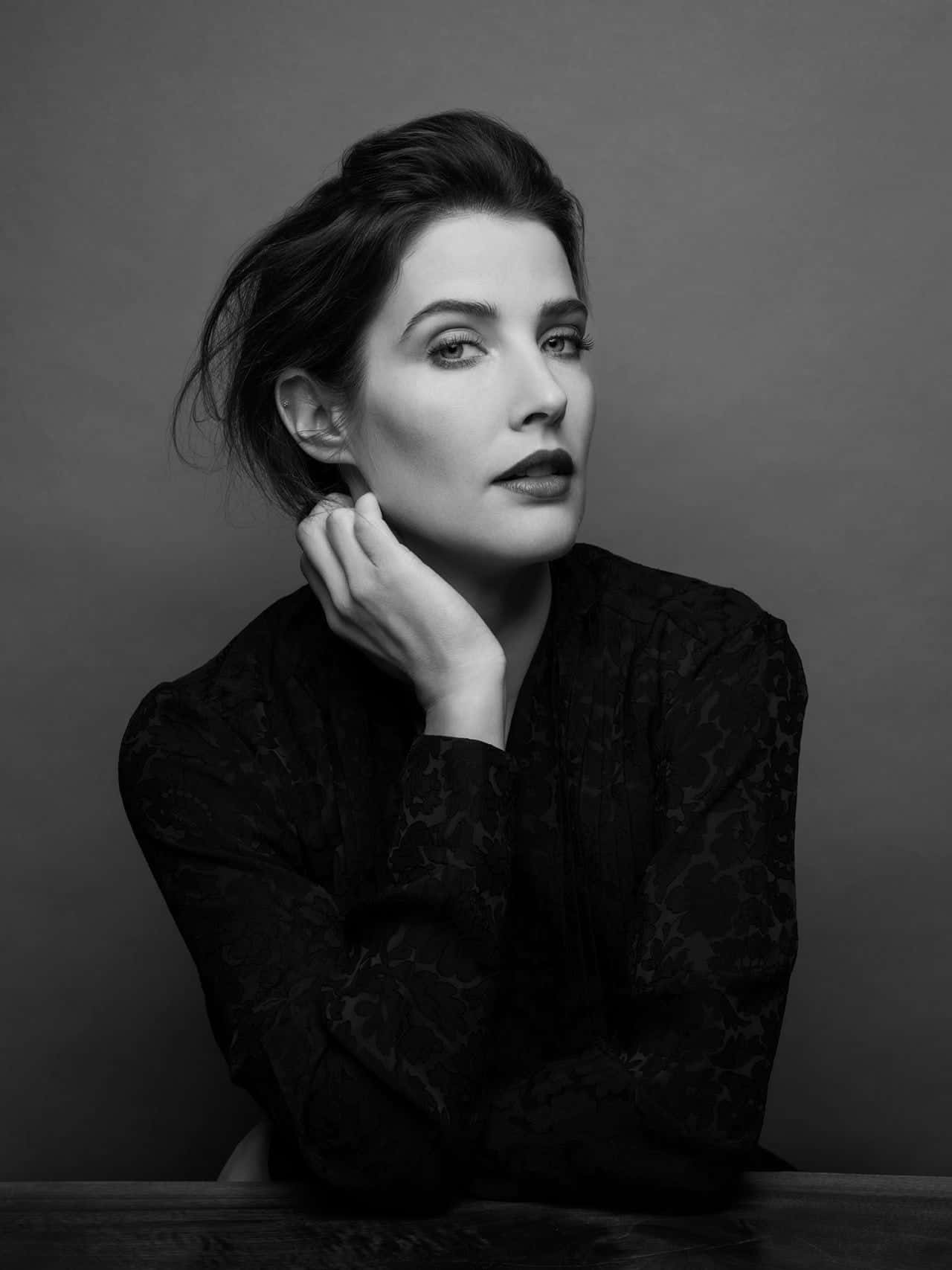 Cobie Smulders 桌布 壁紙 — 一個引人注目的黑白肖像，一位深色頭髮的女性將下巴擱在手上，背景是純灰色。