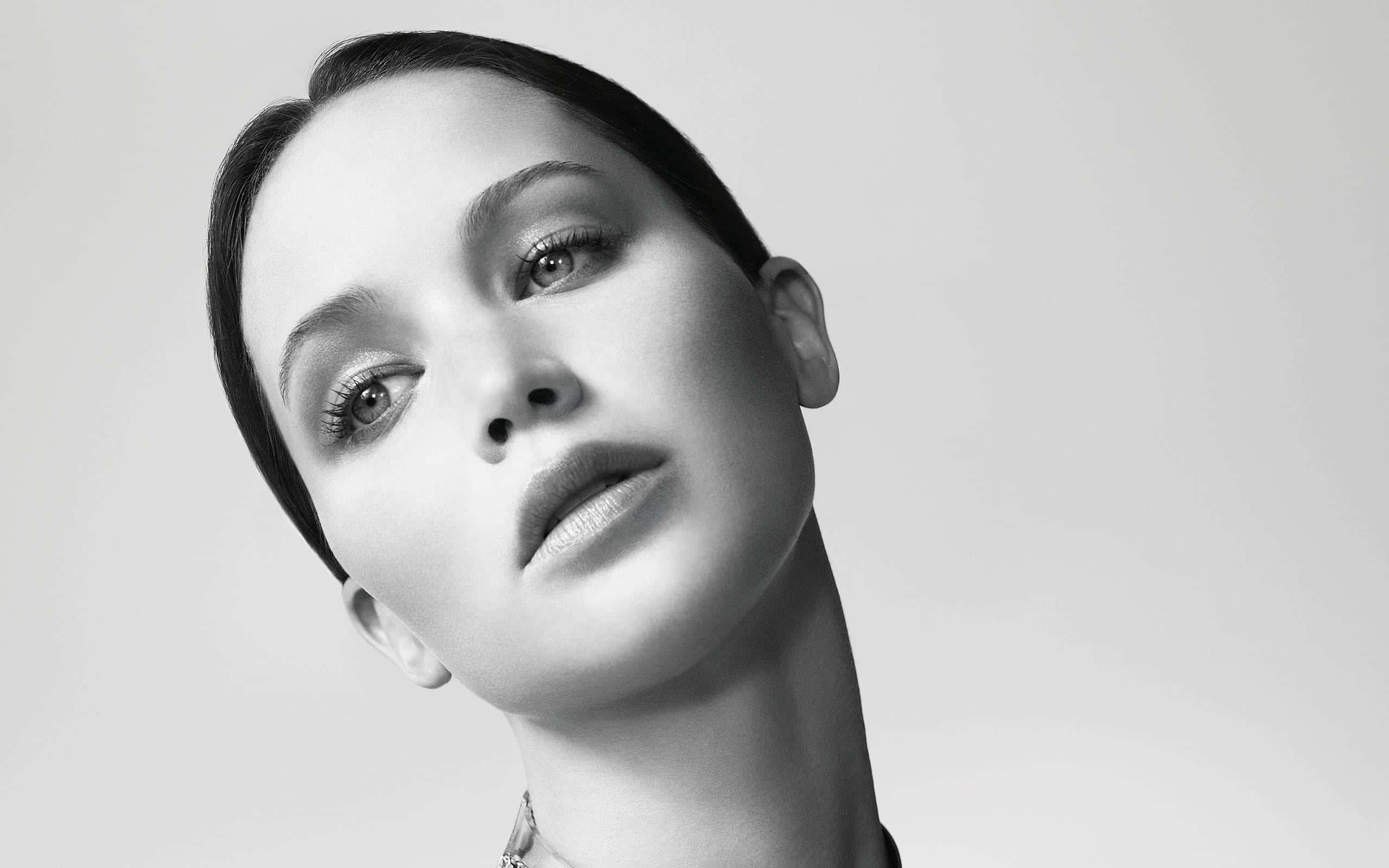 Black And White Celebrity 桌布 壁紙 — 一個引人注目的黑白肖像，一位眼神強烈、頭髮光滑的女性，背景簡潔。