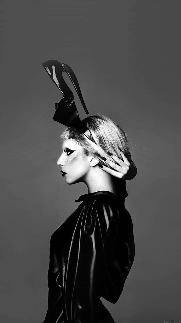Lady Gaga 桌布 壁紙 — 一個引人注目的黑白肖像，側面輪廓的女性戴著光澤黑色帽子和外套，一隻手輕輕觸碰頭部。