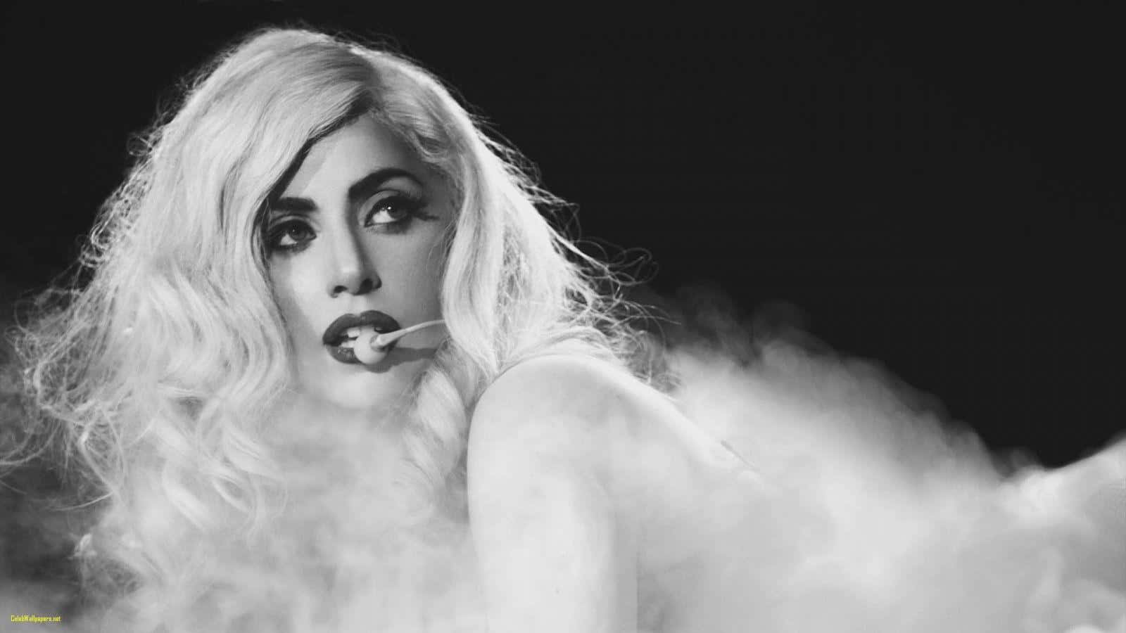 Lady Gaga 桌布 壁紙 — 一個引人注目的黑白肖像，描繪一位擁有豐盈金髮和大膽妝容的女性，在黑暗背景中旋轉的煙霧中手持香煙。