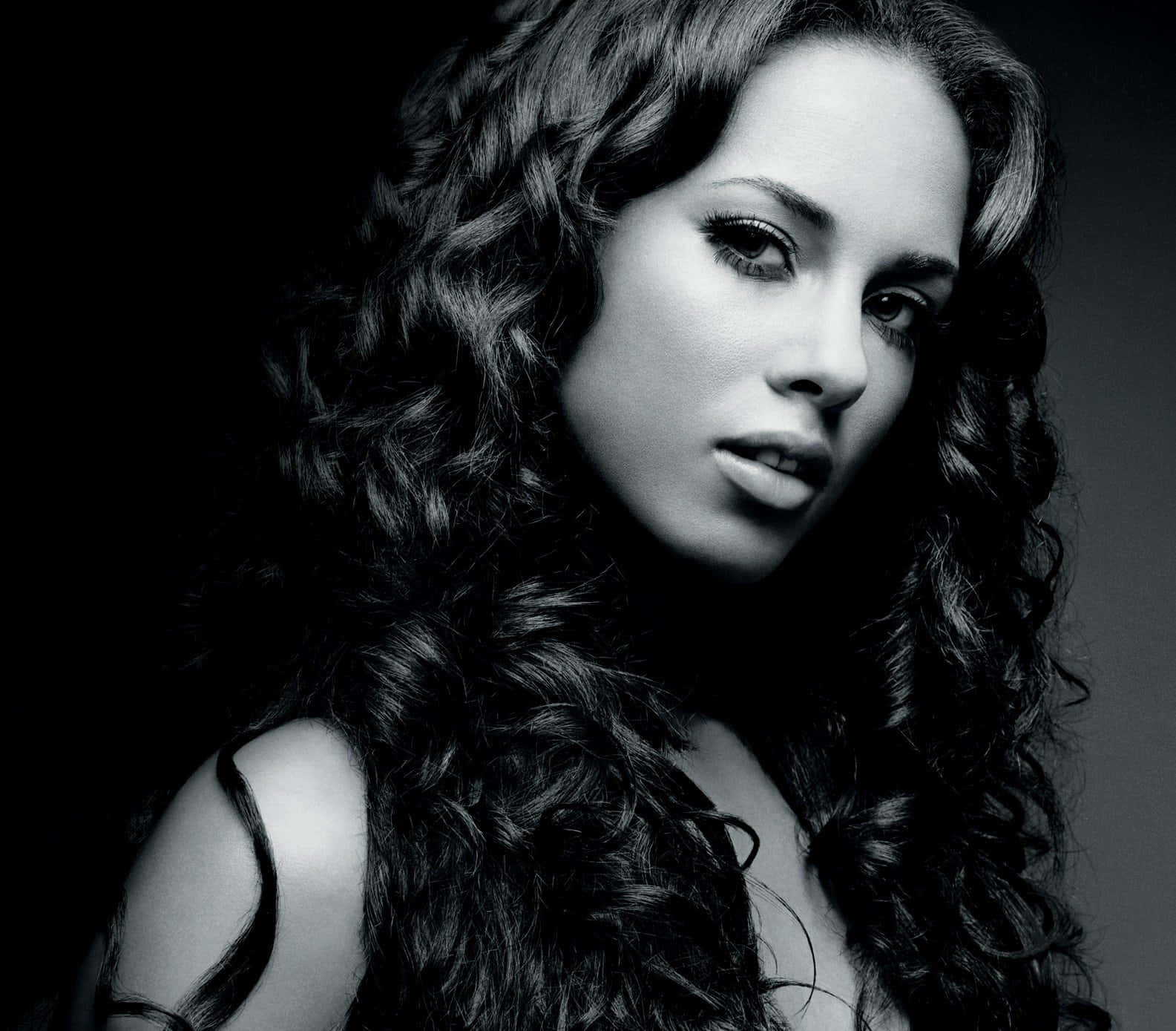Alicia Keys 桌布 壁紙 — 一個引人注目的黑白肖像，描繪一位擁有豐盈捲髮的女性，在深色漸變背景前凝視著。