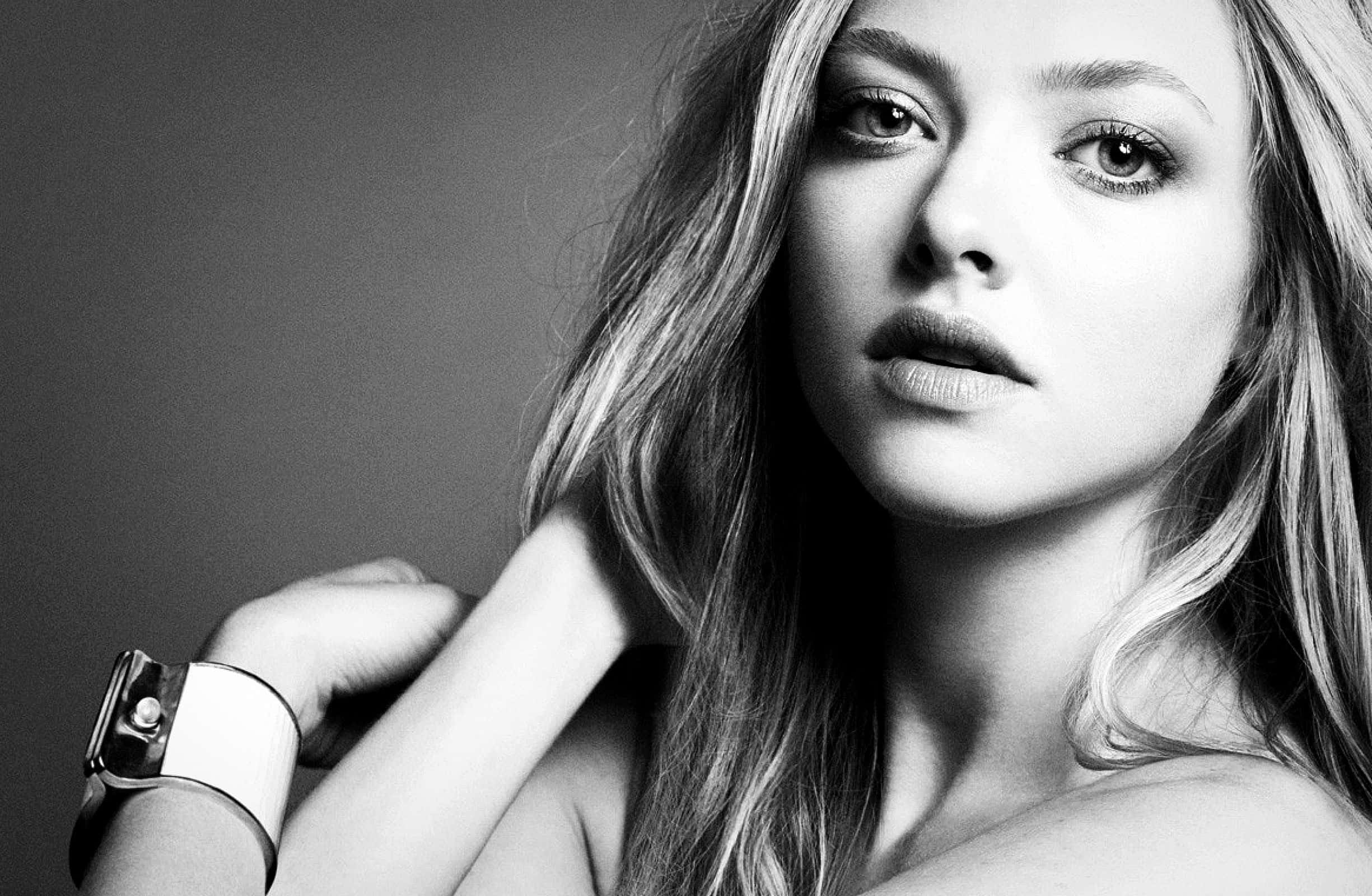 Amanda Seyfried 桌布 壁紙 — 一個引人注目的黑白肖像，長髮女性直視鏡頭，同時觸摸頸部。