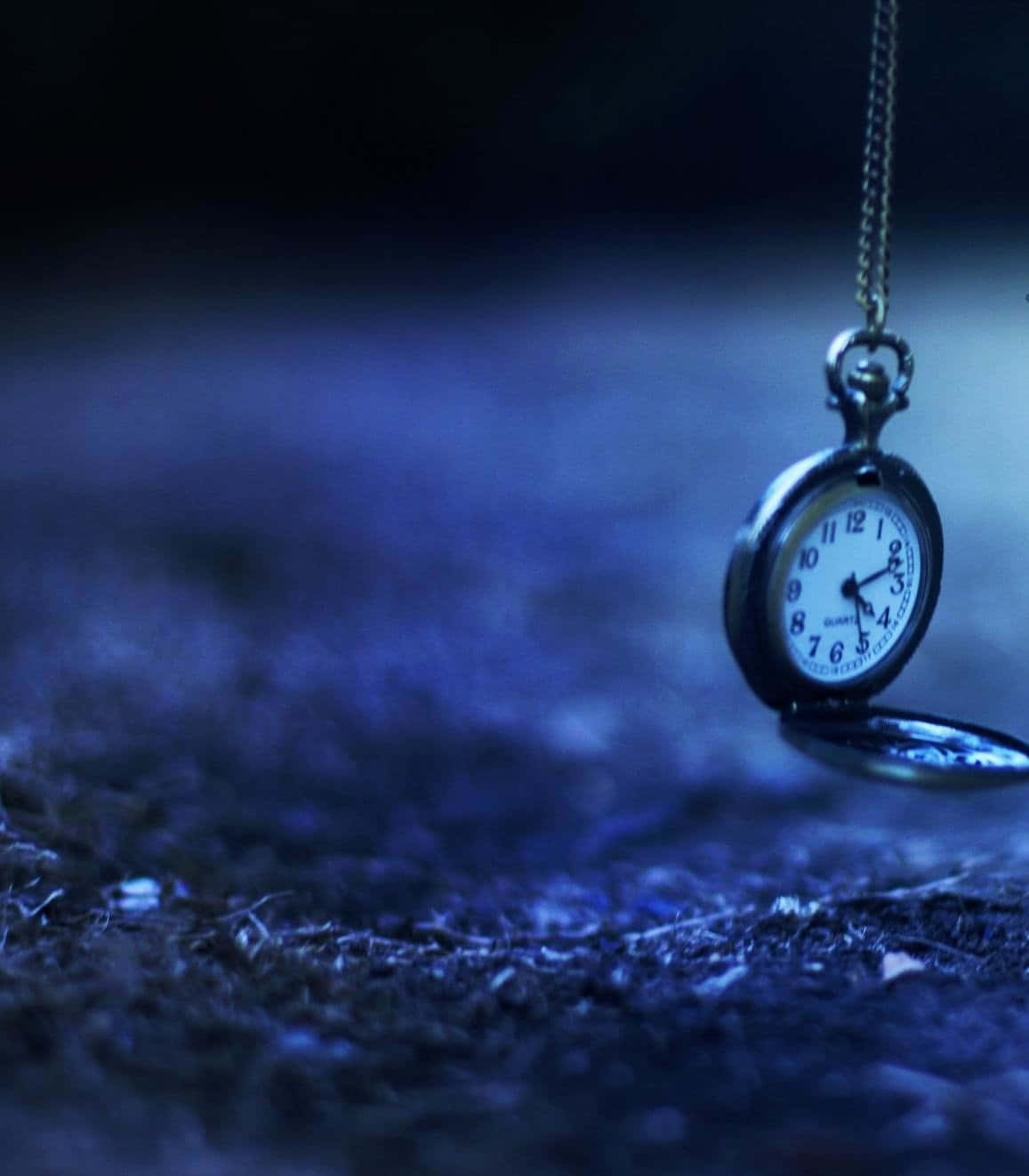 Time 桌布 壁紙 — 一個復古懷錶懸掛在鏈條上，背景是深藍色紋理，在昏暗光線中柔和發光。