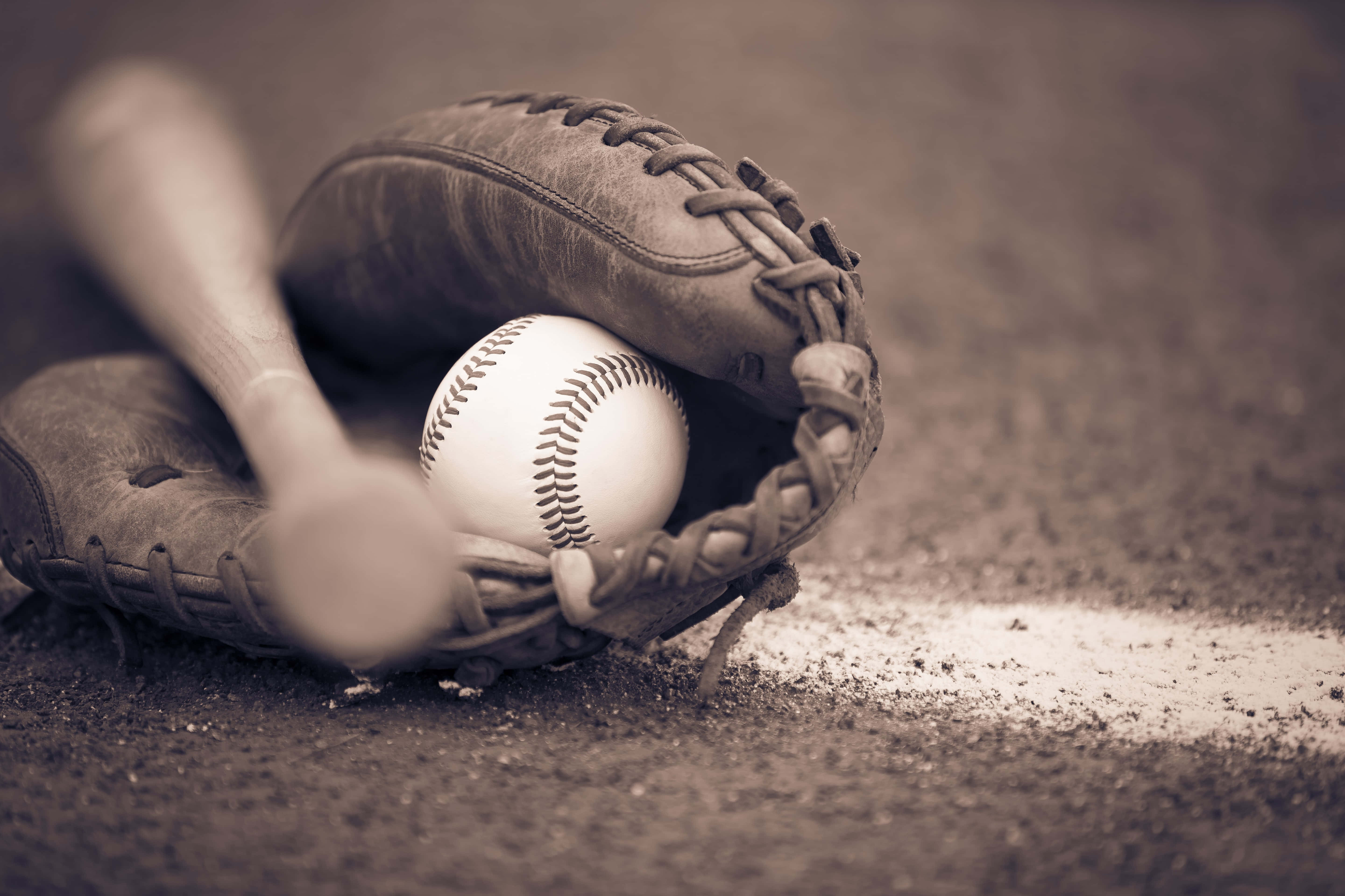 baseball bat 桌布 壁紙 — 一個復古棒球手套托住一個帶紅色縫線的白色棒球，旁邊有一支木製球棒放在塵土飛揚的地面上。