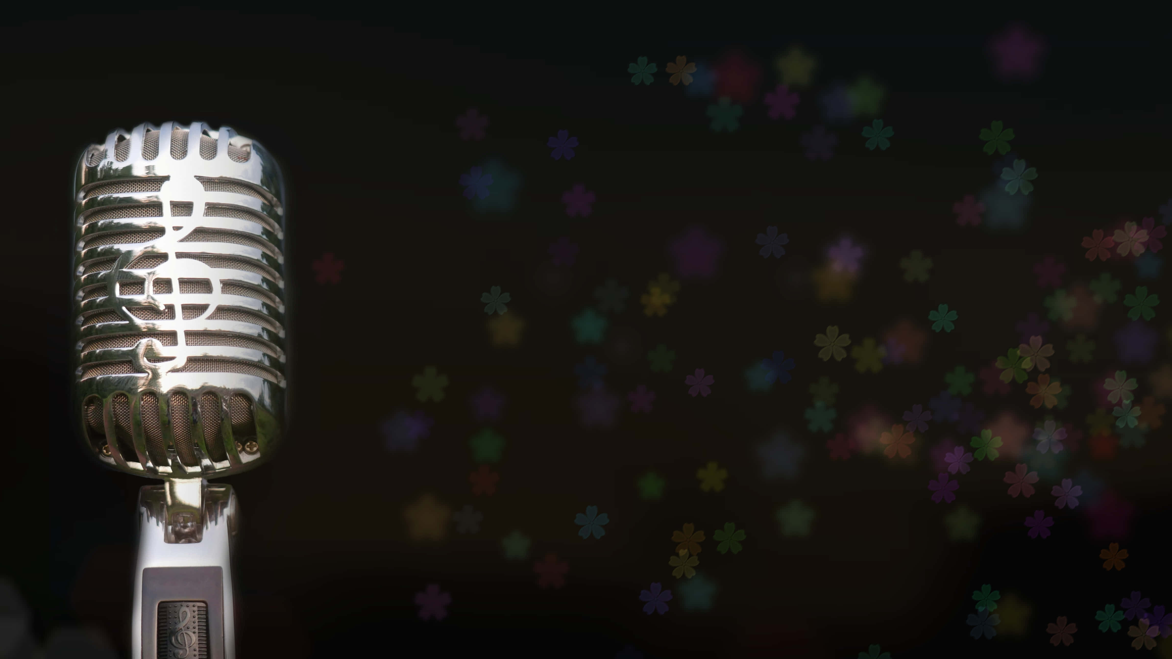 Singer 桌布 壁紙 — 一個復古銀色咪高峰，格柵上刻有高音譜號，立在一個裝飾著色彩繽紛模糊花朵形狀的黑暗背景前。