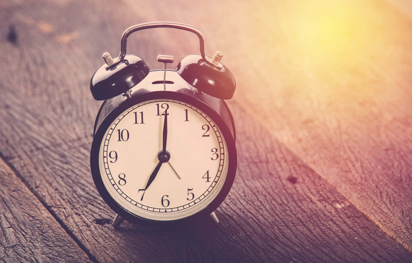 Time 桌布 壁紙 — 一個復古黑色鬧鐘（帶鈴鐺）放在一個經風化的木質表面上，沐浴在溫暖的金色陽光中。