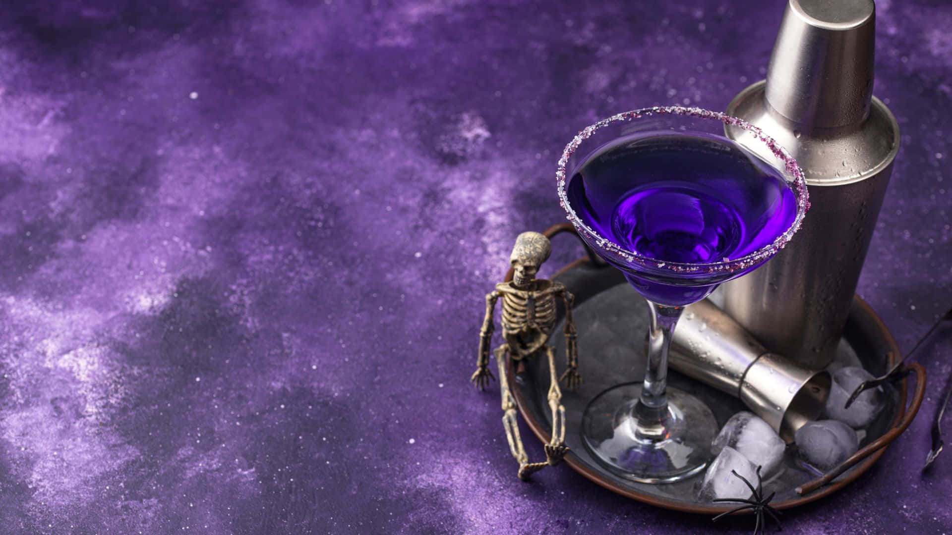 Spooky Cocktails 桌布 壁紙 — 一個微型骷髏坐在一個金屬托盤上，旁邊是一杯帶有糖邊的鮮豔紫色雞尾酒，背景是宇宙紫色紋理背景。