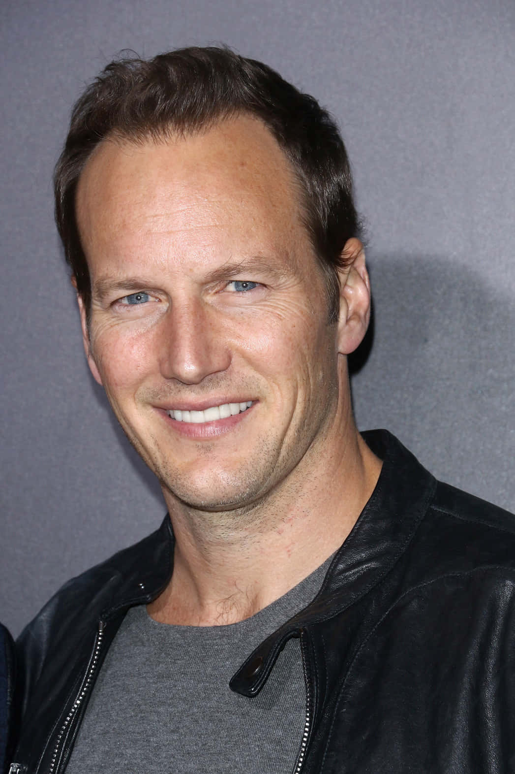 Patrick Wilson 桌布 壁紙 — 一個微笑嘅男人嘅近距離肖像，佢有藍色眼睛，喺灰色背景前著住一件黑色皮褸同灰色恤衫。