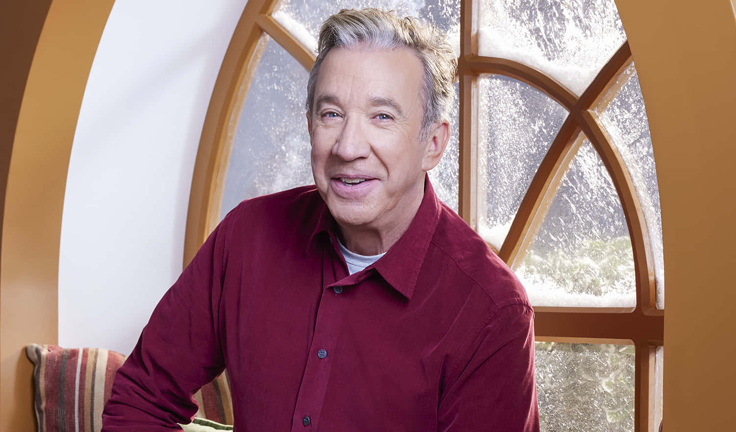 Tim Allen 桌布 壁紙 — 一個微笑嘅男人着住紅色恤衫，坐喺一個有磨砂玻璃板嘅大拱形窗旁邊。