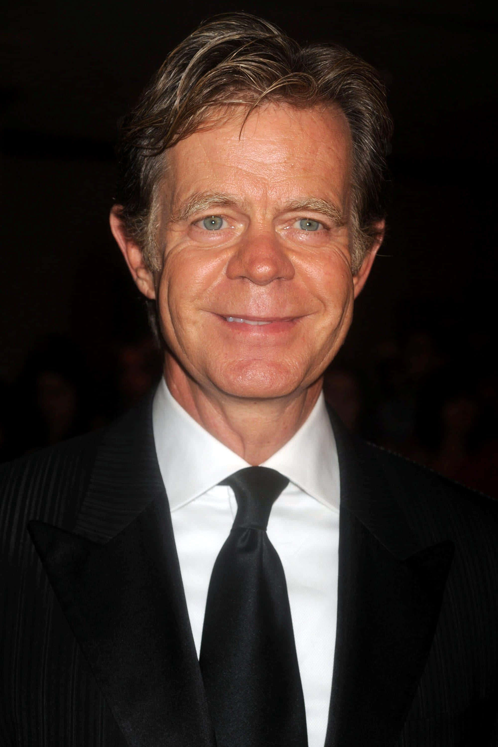 william h. macy 桌布 壁紙 — 一個微笑男士的close-up肖像，身穿黑色細條紋西裝和白色襯衫，背景是深色模糊的。