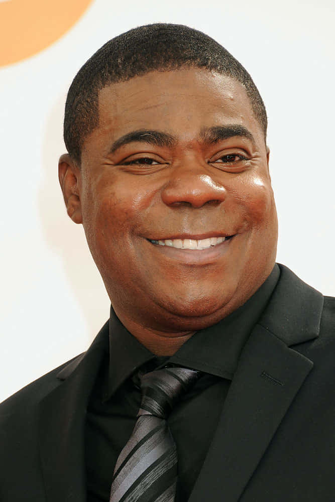 Tracy Morgan 桌布 壁紙 — 一個微笑男士的頭像特寫，身穿黑色西裝和條紋領帶，背景明亮。
