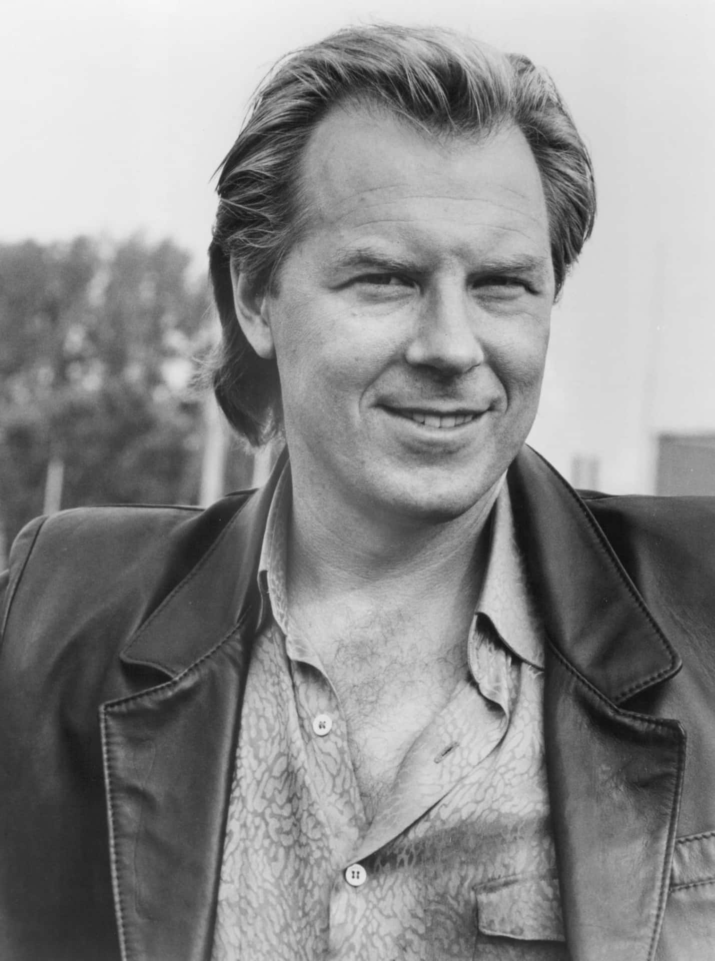 Michael Mckean 桌布 壁紙 — 一個微笑男士的黑色肖像，他梳著時尚髮型，身穿皮褸內搭圖案恤衫。