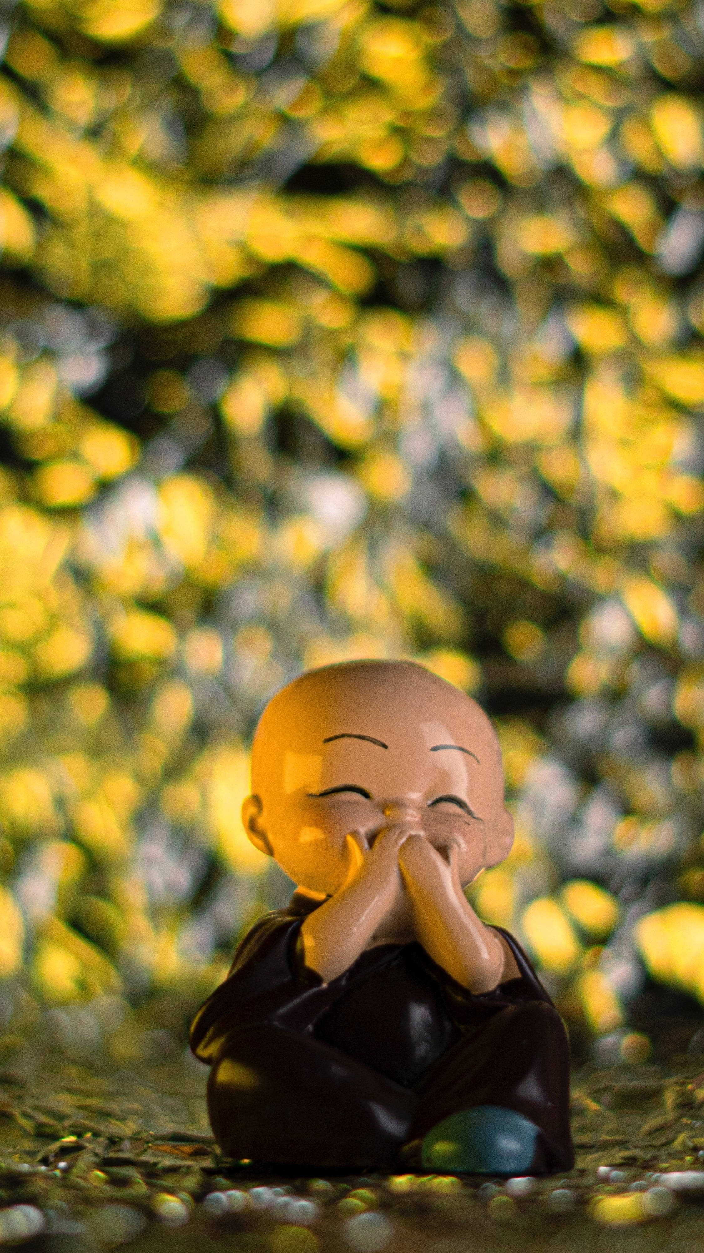 Statue Aesthetic 桌布 壁紙 — 一個微笑的小佛像盤腿坐在鵝卵石上，背景是金色的散景樹葉。