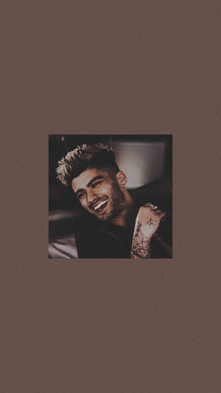 Zayn Malik 桌布 壁紙 — 一個微笑的男人，擁有造型頭髮和手臂上的紋身，以柔和的棕色背景襯托。