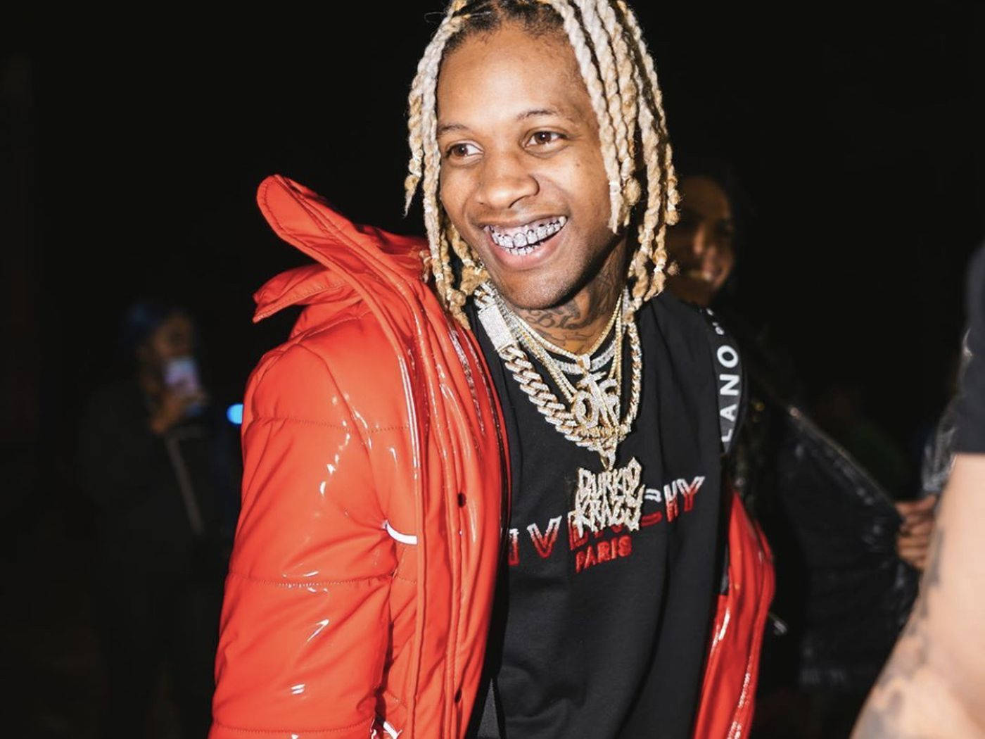 King Von And Lil Durk 桌布 壁紙 — 一個微笑的男人，辮子頭髮，穿著閃亮的紅色外套和金色鏈條，背景是黑暗的夜晚。