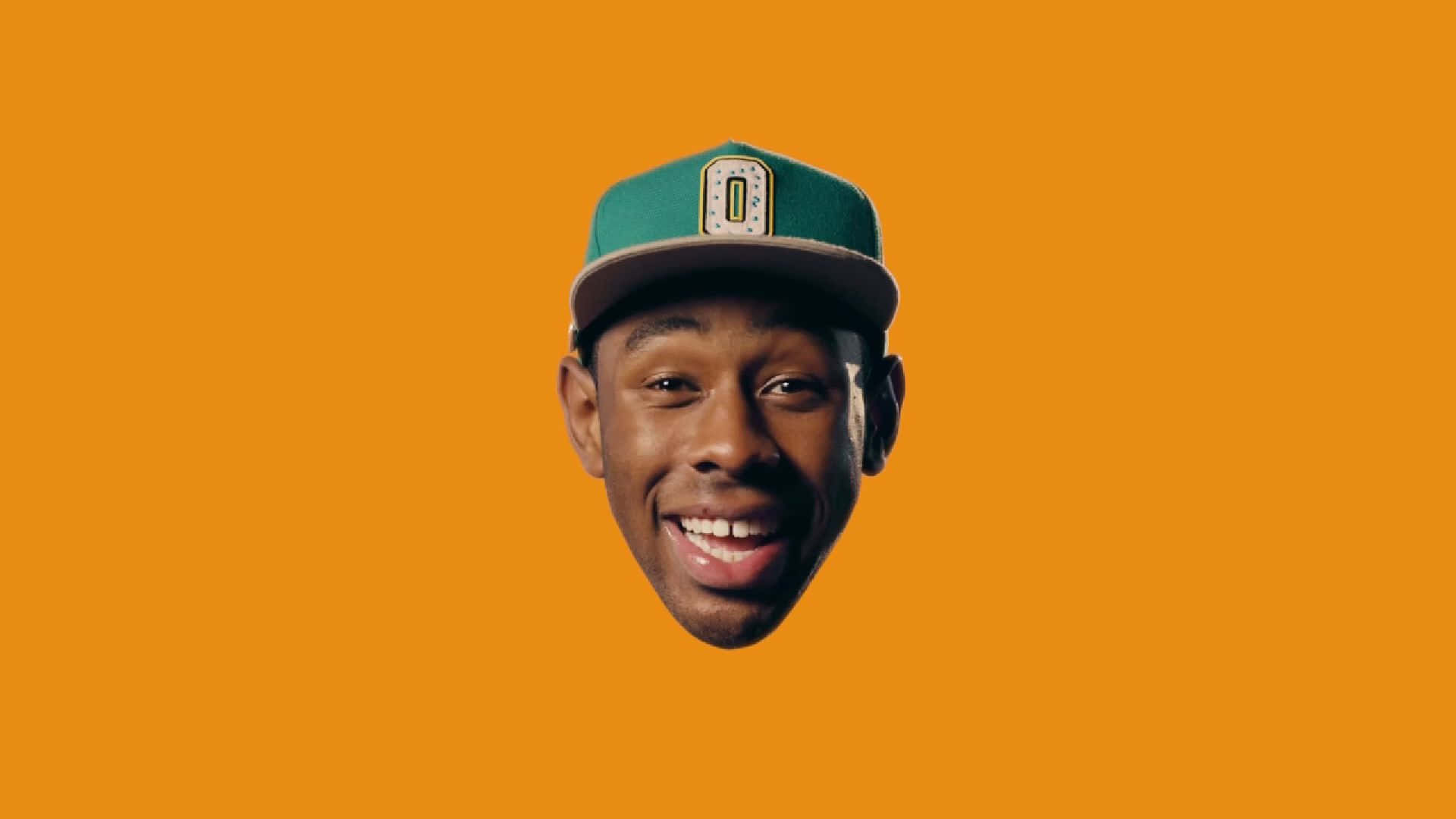tyler the creator 桌布 壁紙 — 一個微笑的男人戴著綠色棒球帽，漂浮在純橙色背景上。