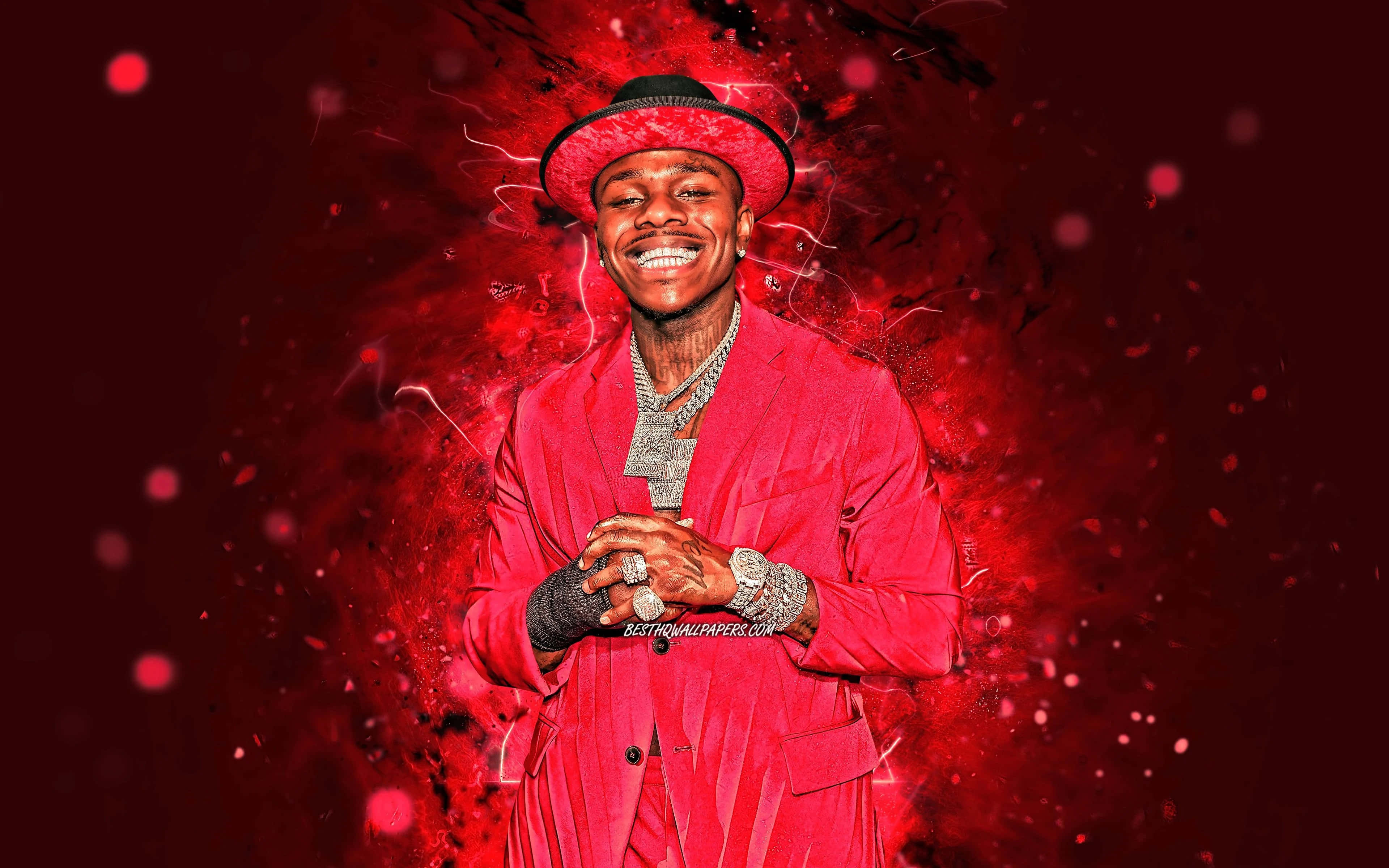 Dababy 桌布 壁紙 — 一個微笑的男人穿著紅色西裝和帽子，在充滿發光粒子的鮮豔紅色抽象背景前散發能量。
