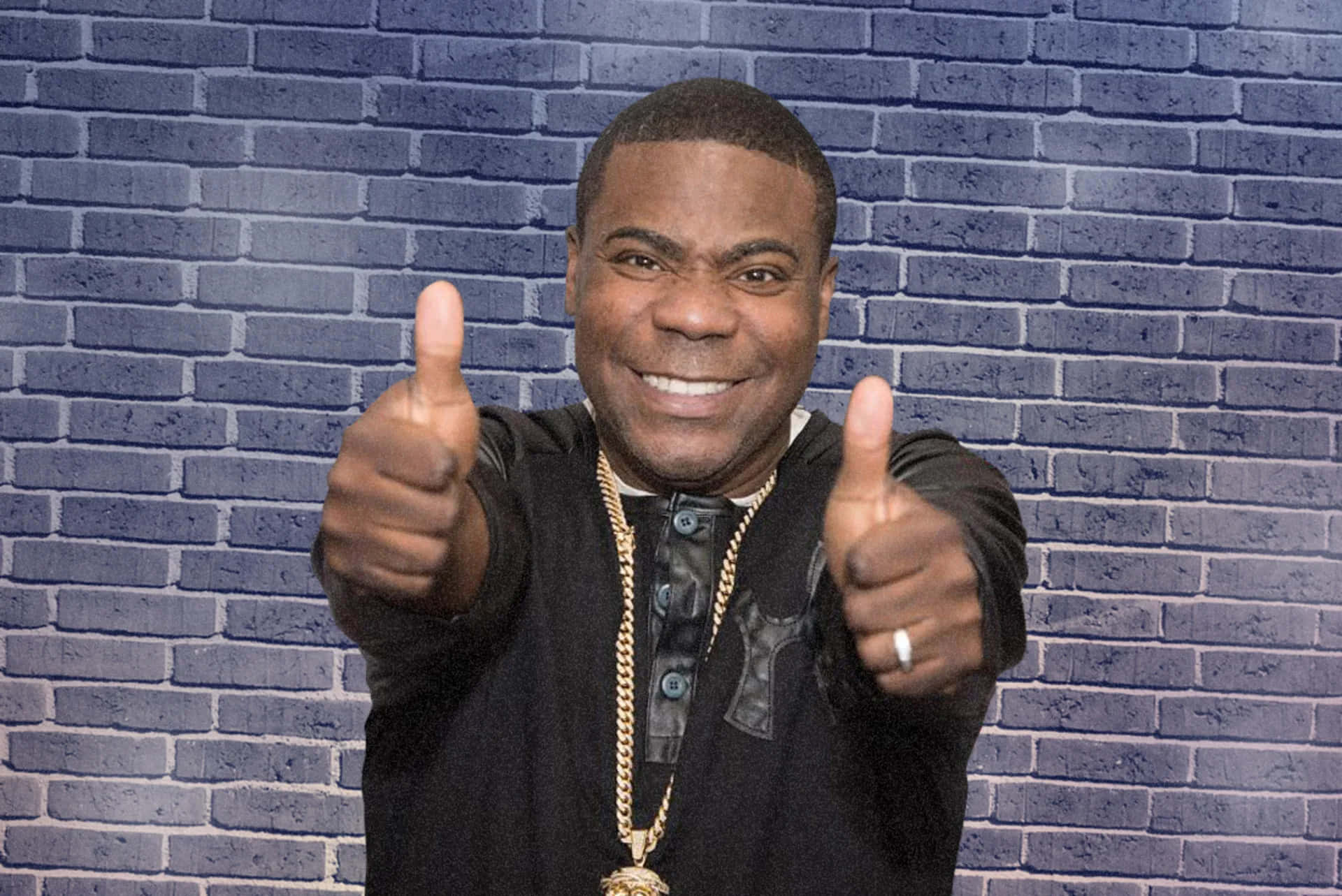 Tracy Morgan 桌布 壁紙 — 一個微笑的男人穿著黑色外套，在藍色磚牆背景前豎起兩個大拇指。
