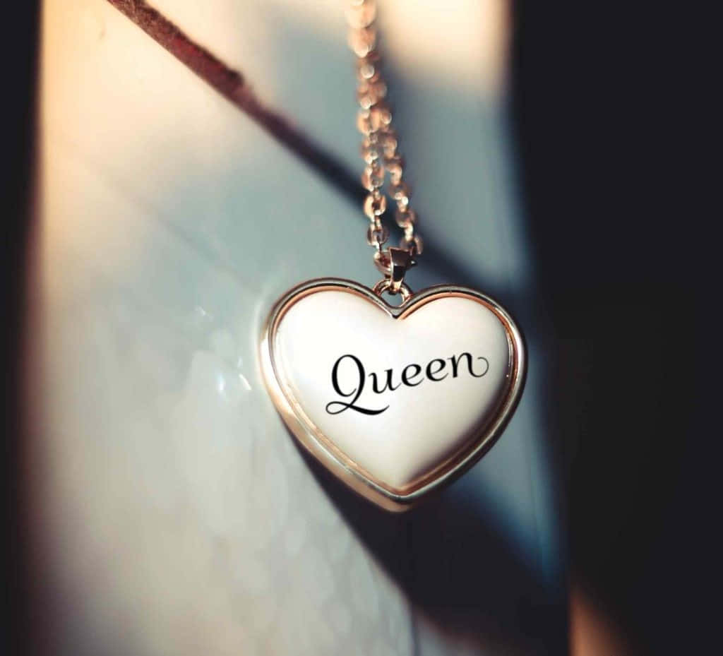 女王 桌布 壁紙 — 一個心形吊墜，上面以草書刻有Queen字樣，掛在一條鏈條上，背景是柔和光線下的大理石。