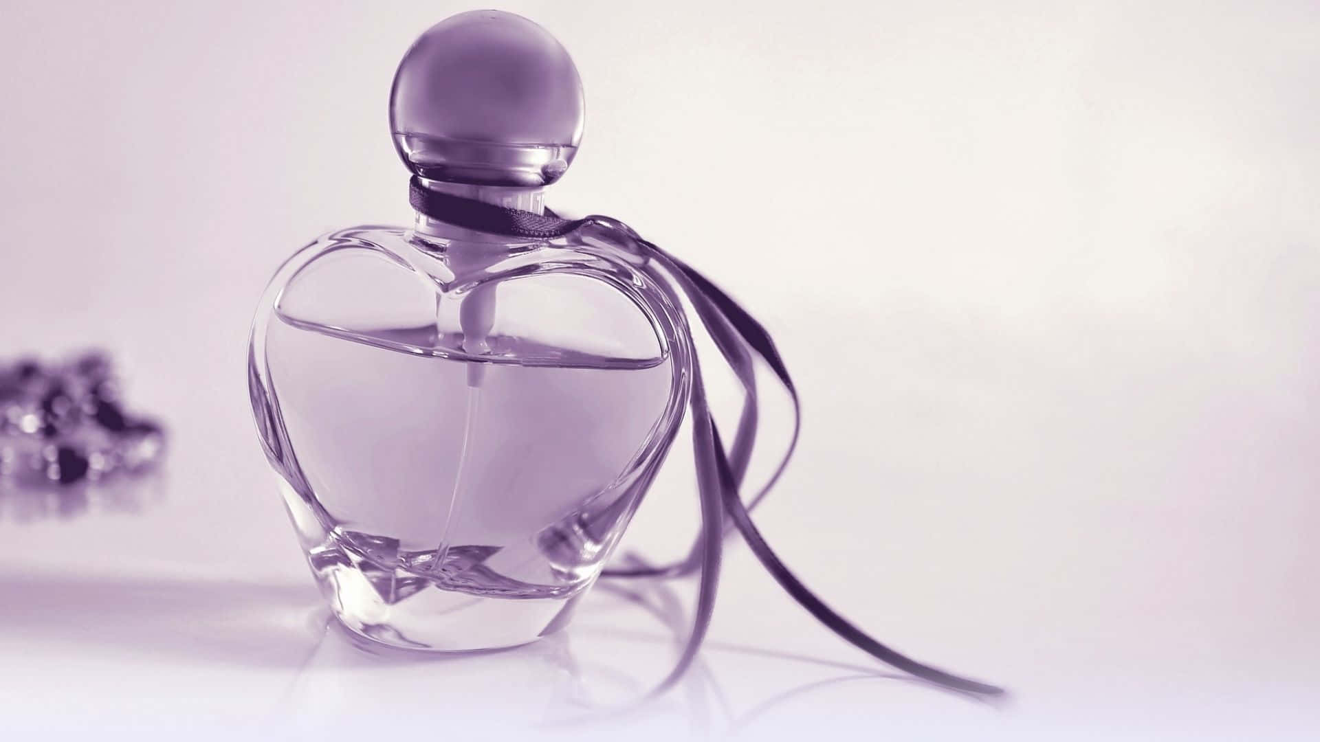 Fragrance 桌布 壁紙 — 一個心形玻璃香水瓶，帶有紫色絲帶，優雅地放置在反射表面上，背景是柔和的薰衣草色。