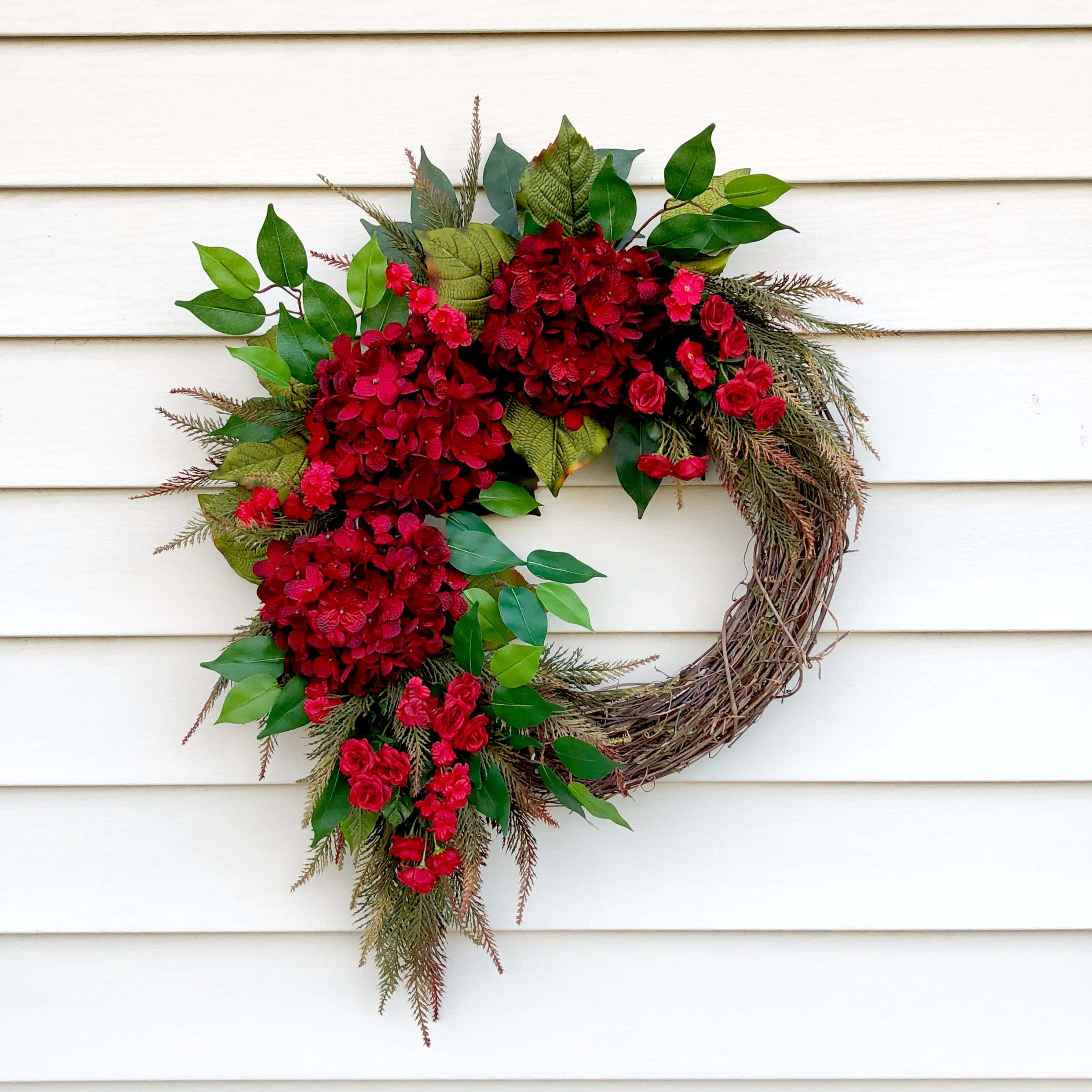 Spring Wreaths 桌布 壁紙 — 一個心形花環，飾有紅色繡球花、玫瑰和綠色葉子，掛在白色木門上。