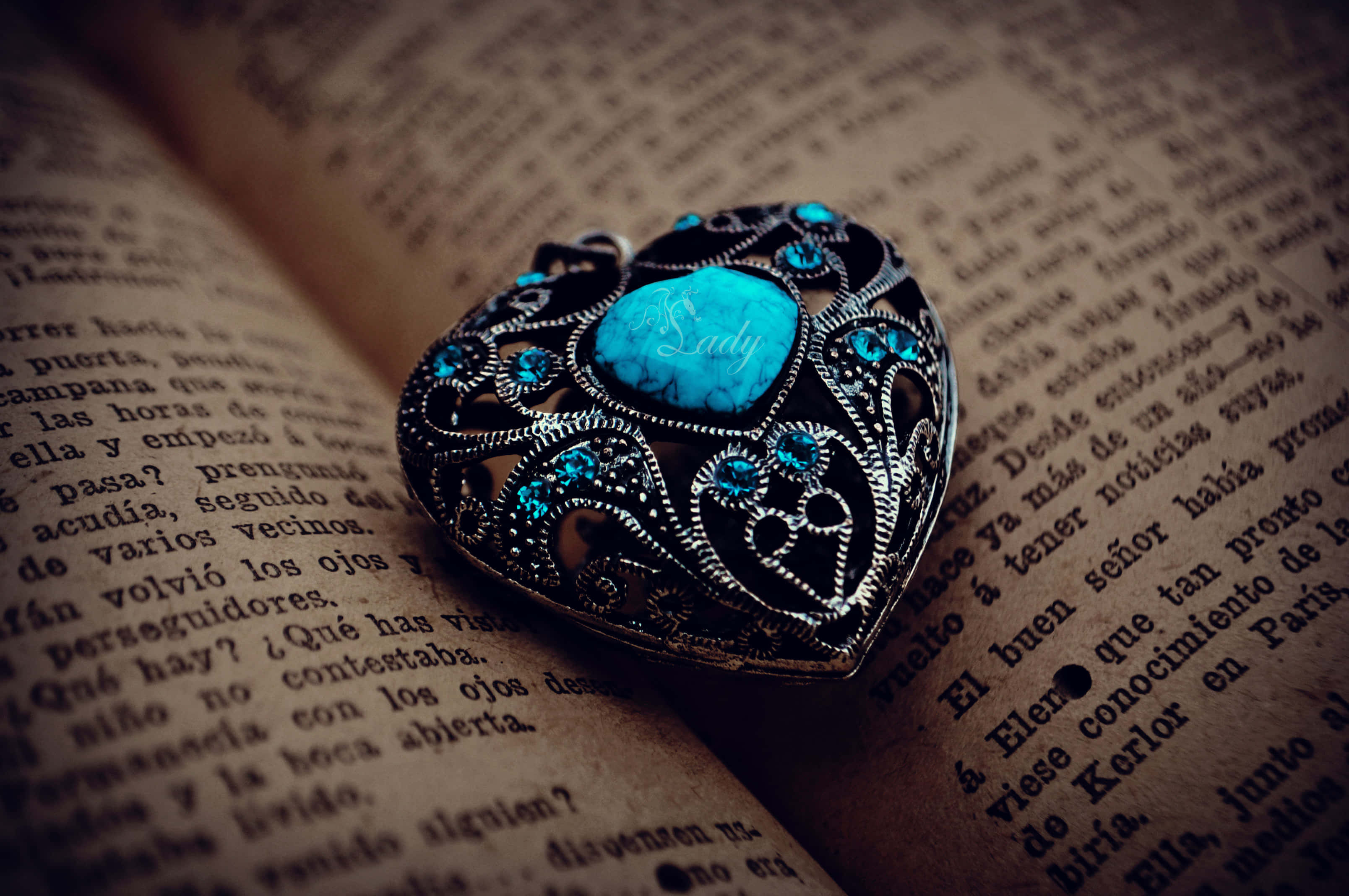 Jewelry Design 桌布 壁紙 — 一個心形鏤空吊墜，鑲有綠松石，優雅地放在一本打開的復古書頁上。