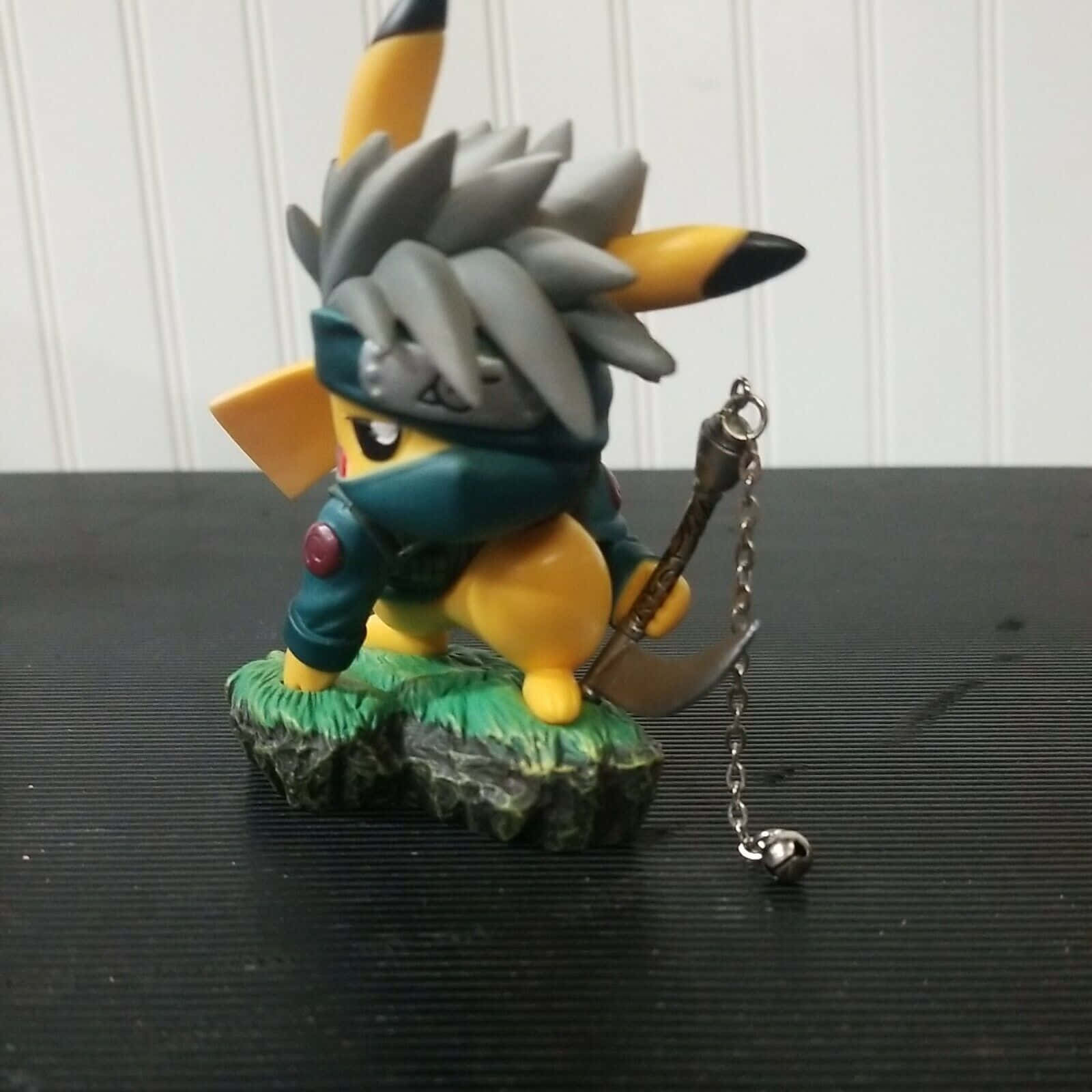 Pokemon Figures 桌布 壁紙 — 一個忍者主題的比卡超公仔，灰色尖刺頭髮和藍色面具，站在岩石底座上，手持鏈條武器。