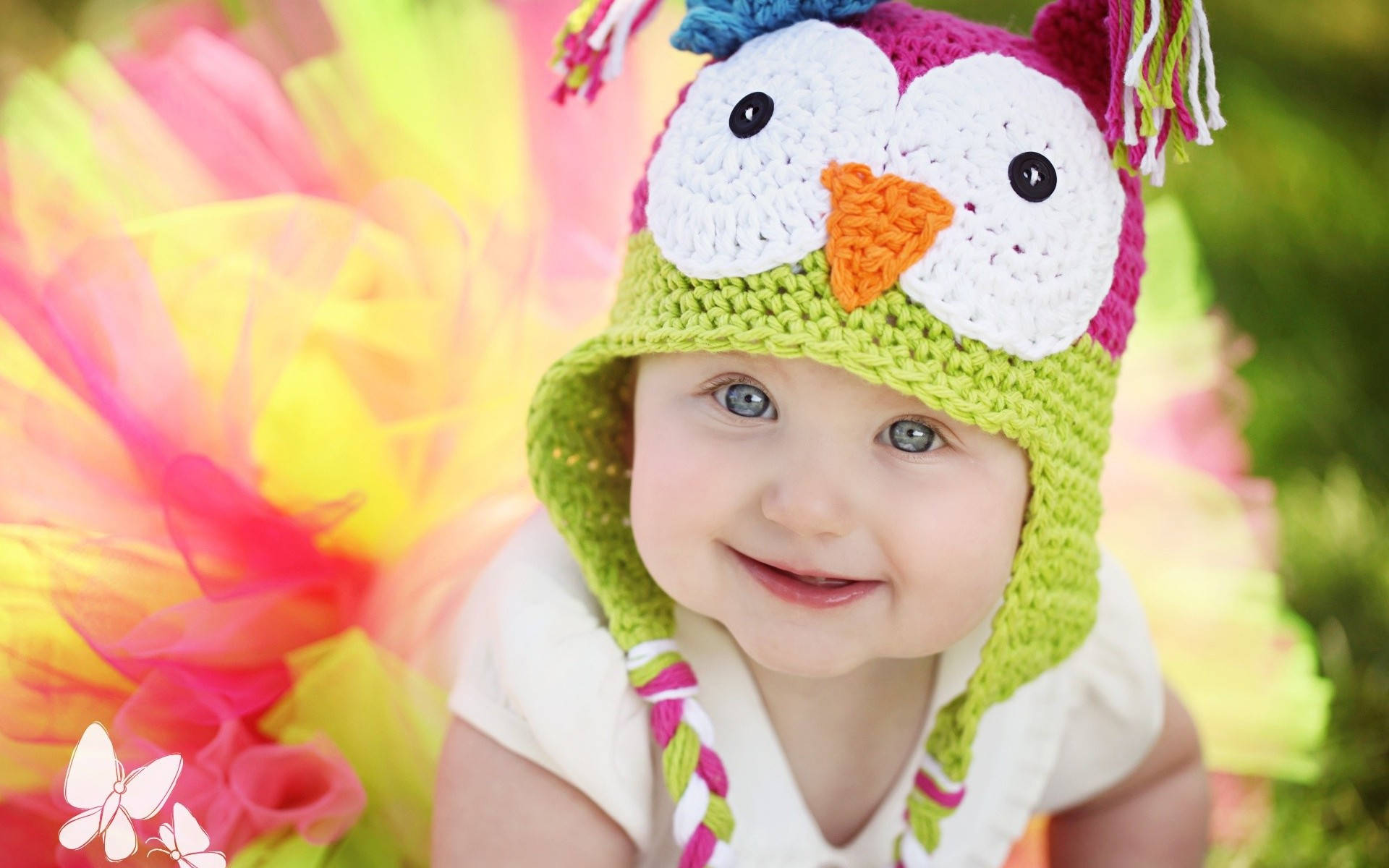 Baby Girl 桌布 壁紙 — 一個快樂的嬰兒戴著色彩繽紛的鉤織貓頭鷹帽，在充滿活力的薄紗背景下燦爛地微笑。